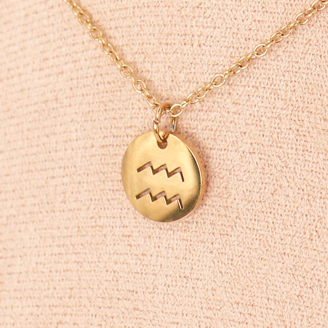 Pendentif rond en acier inoxydable représentant un signe du zodiaque, suspendu à un cordon en cuir, élégant et moderne.