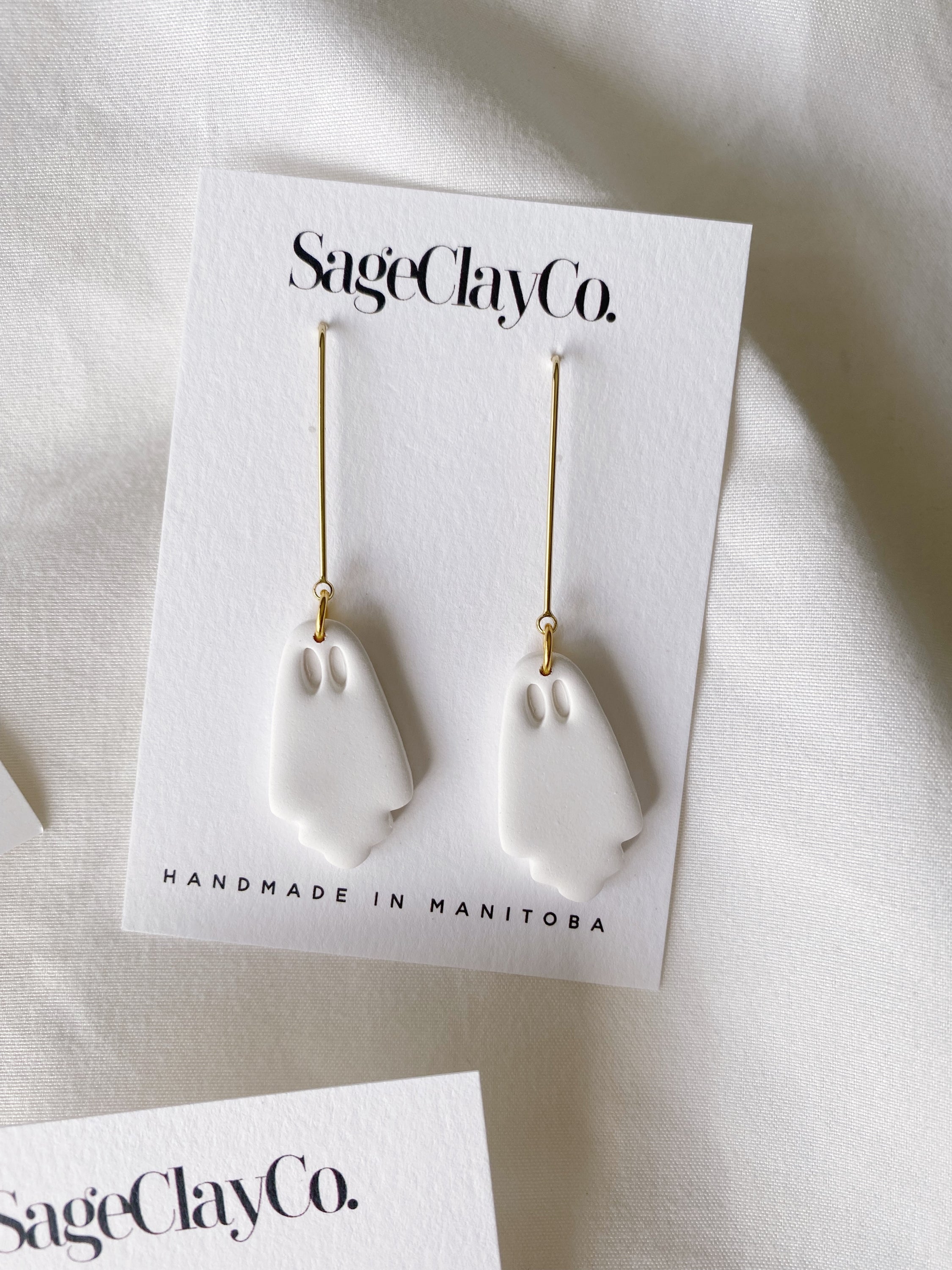 A pair of Ghost Drops handmade polymer clay earrings featuring a minimalist pumpkin dangle design, showcasing unique craftsmanship.