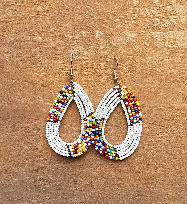 Elegant white handmade Maasai beaded drop and dangle earrings, featuring a unique oval shape and colorful bead accents.