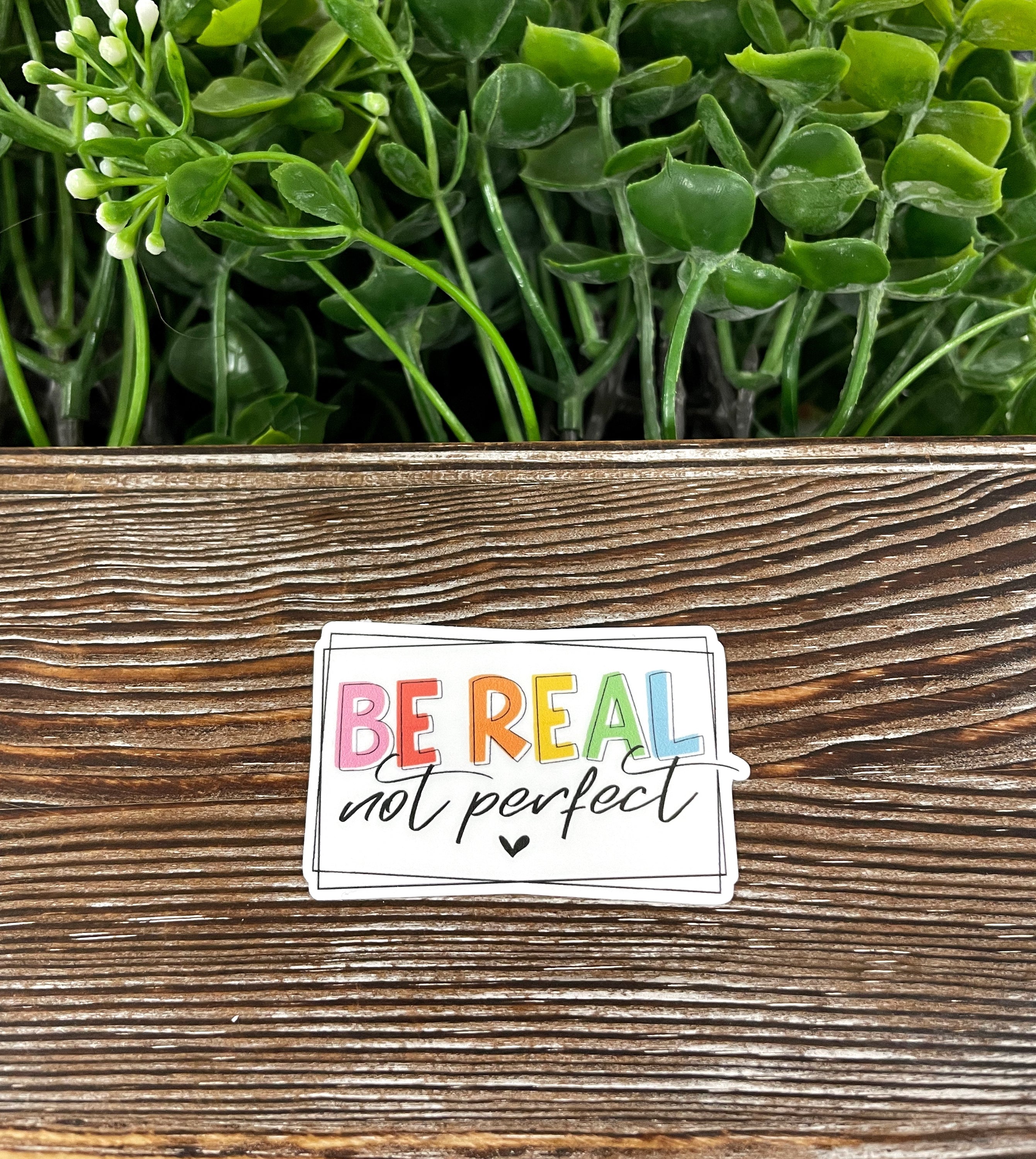 Be Real Not Perfect die cut vinyl sticker on a smooth surface, showcasing its vibrant colors and water-resistant laminate finish.