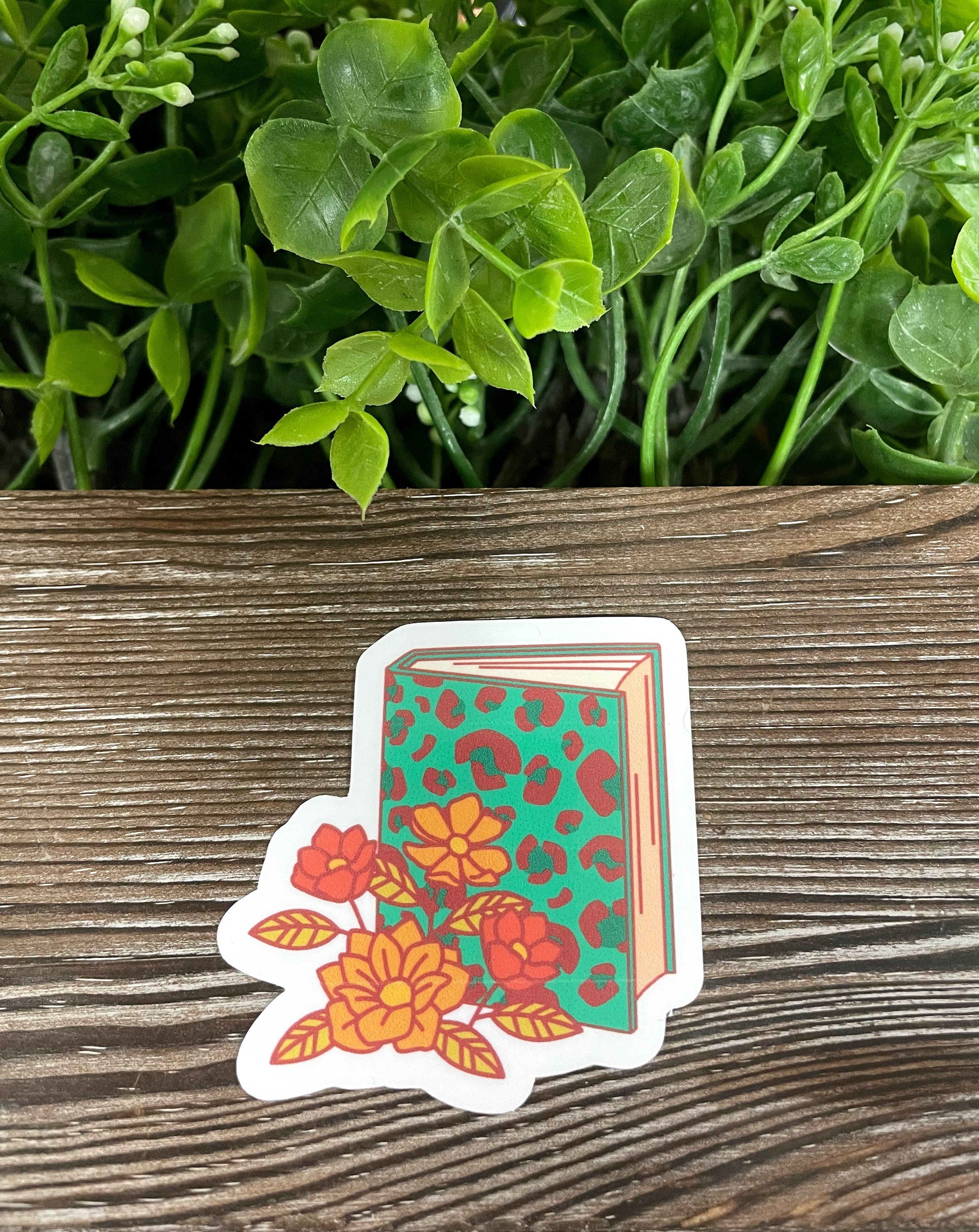 Blue Cheetah Book and Flowers die cut vinyl sticker on a smooth surface, showcasing vibrant colors and intricate design.