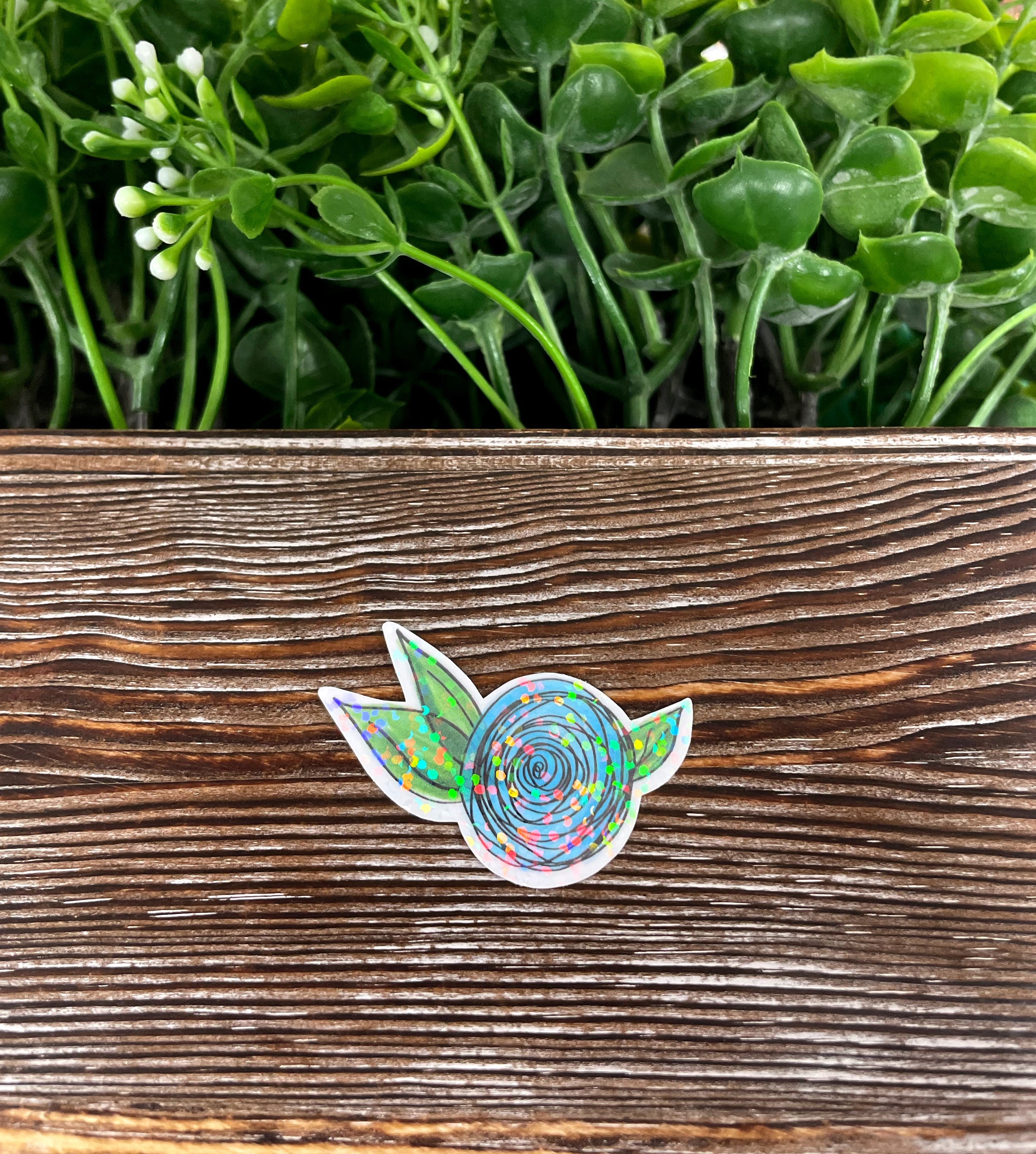 A vibrant blue watercolor flower die cut vinyl sticker on a smooth surface, showcasing its intricate design and water-resistant laminate finish.