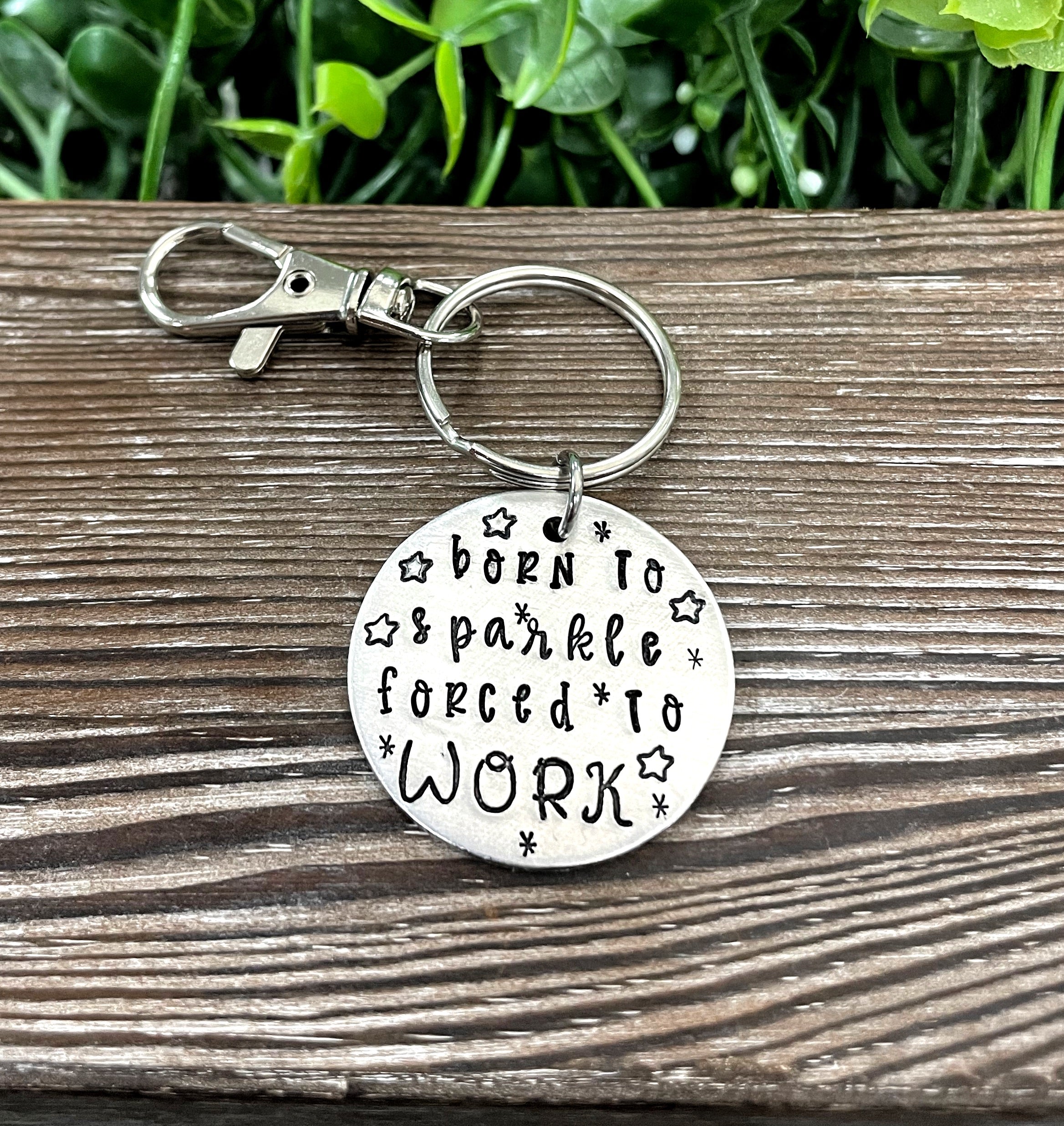 A hand-stamped keychain featuring the quote 'Born to sparkle forced to work', showcasing unique letter spacing and design.