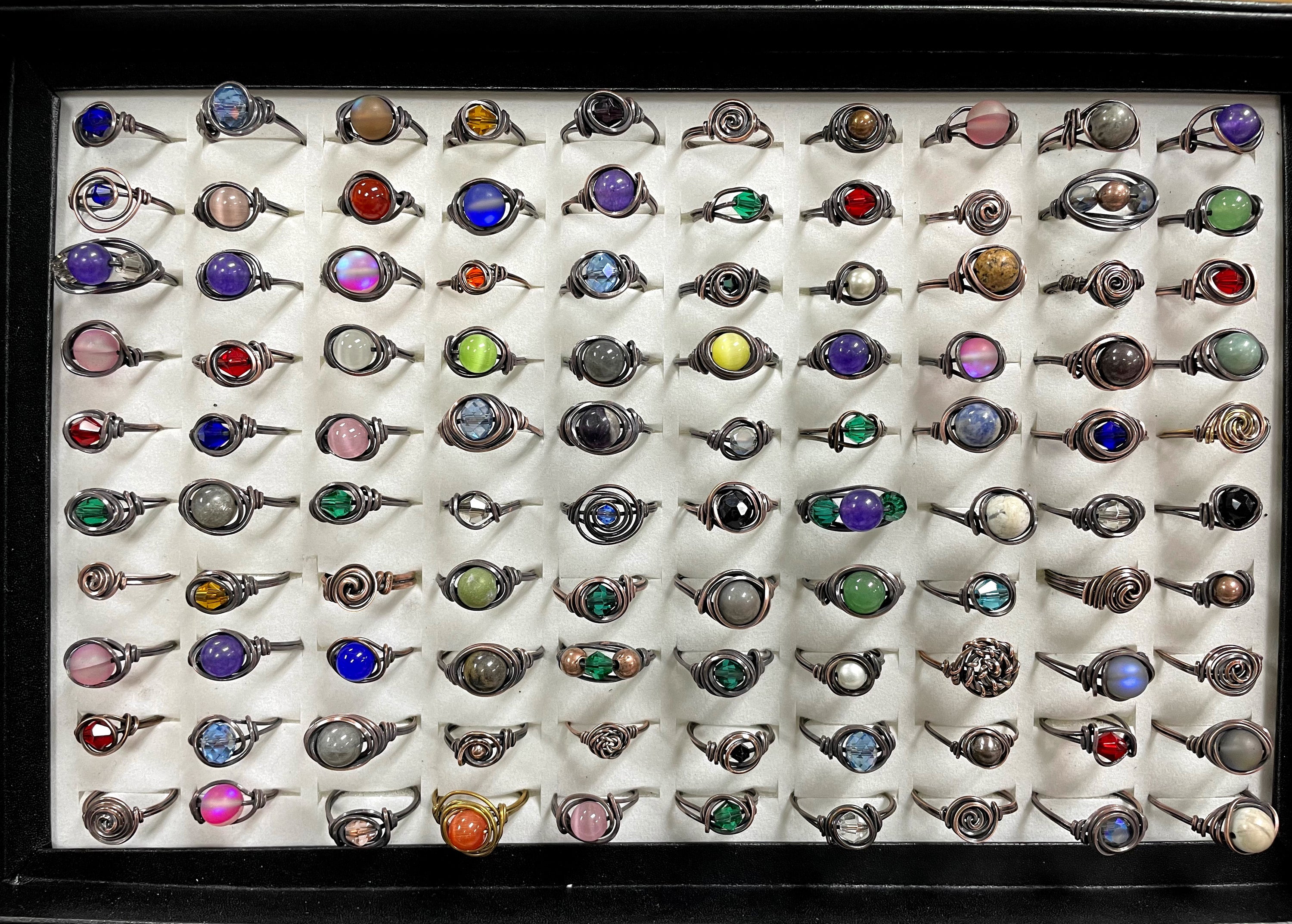 A collection of 100 wire wrapped rings featuring various gemstones and glass beads, showcasing their unique designs and antique finish.