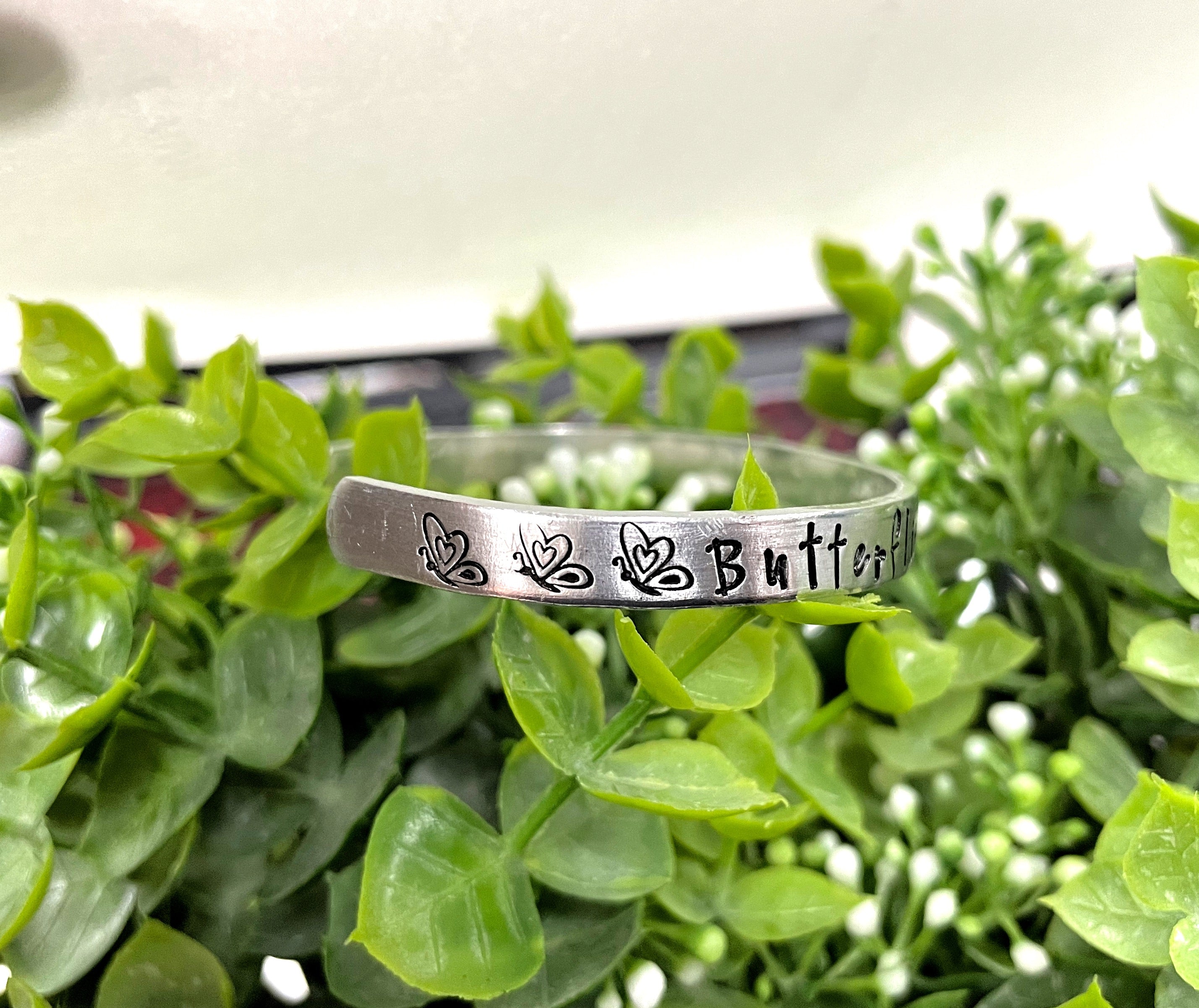 Hand-stamped aluminum cuff bracelet with the phrase 'Butterflies Appear when Angels are Near', showcasing unique letter variations.