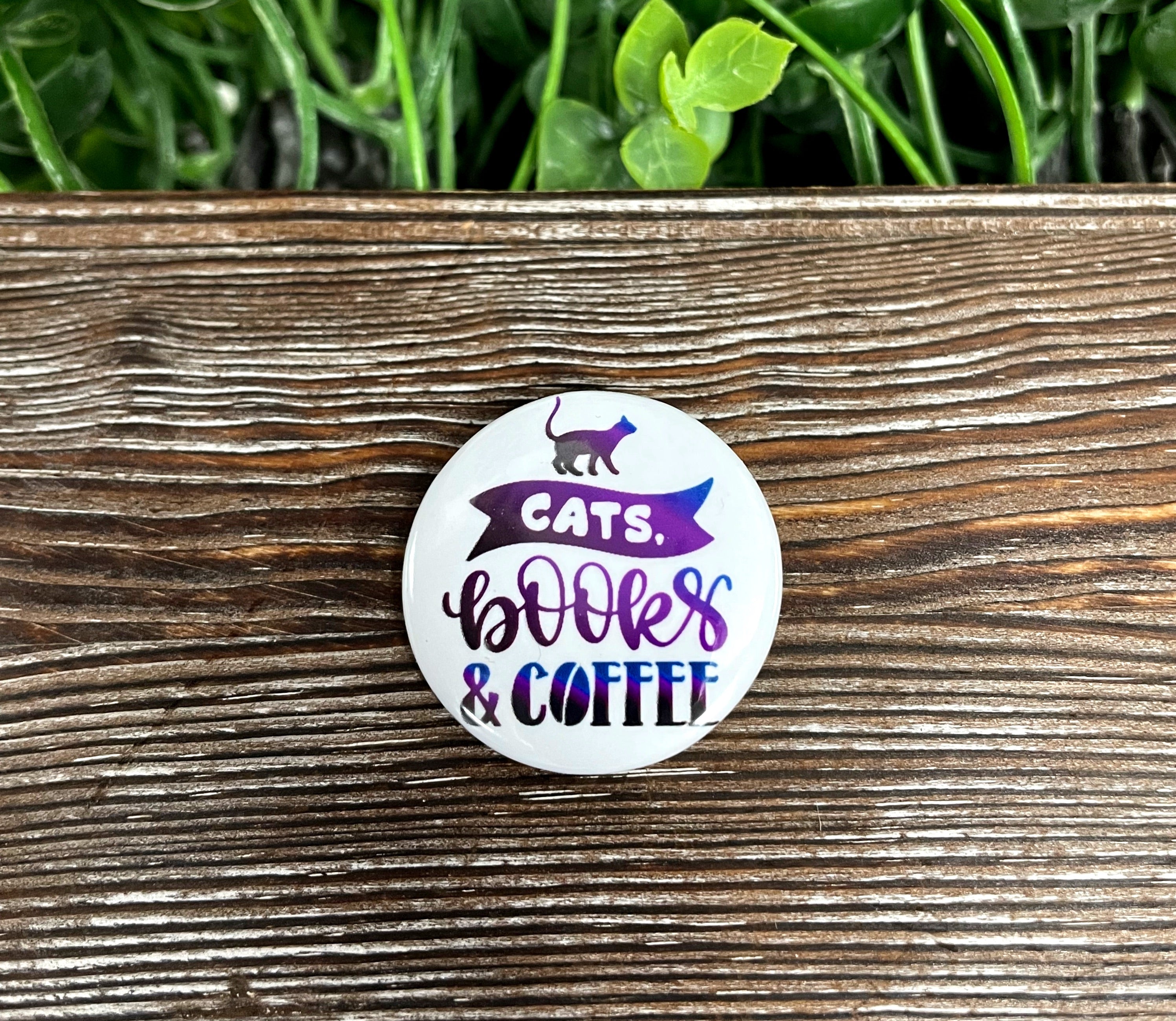 A vibrant purple graphic art button featuring cats, books, and coffee, measuring 1.25 inches, perfect for personalizing bags and accessories.