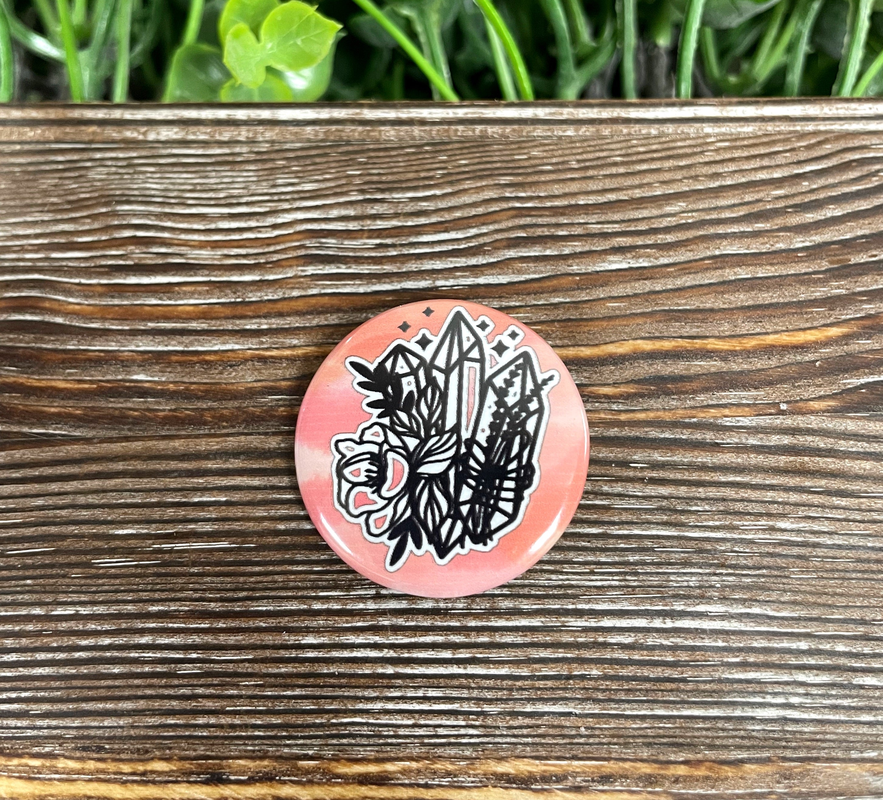A 1.25-inch graphic art button featuring a colorful crystals and flowers design on a pink background, perfect for personalizing accessories.