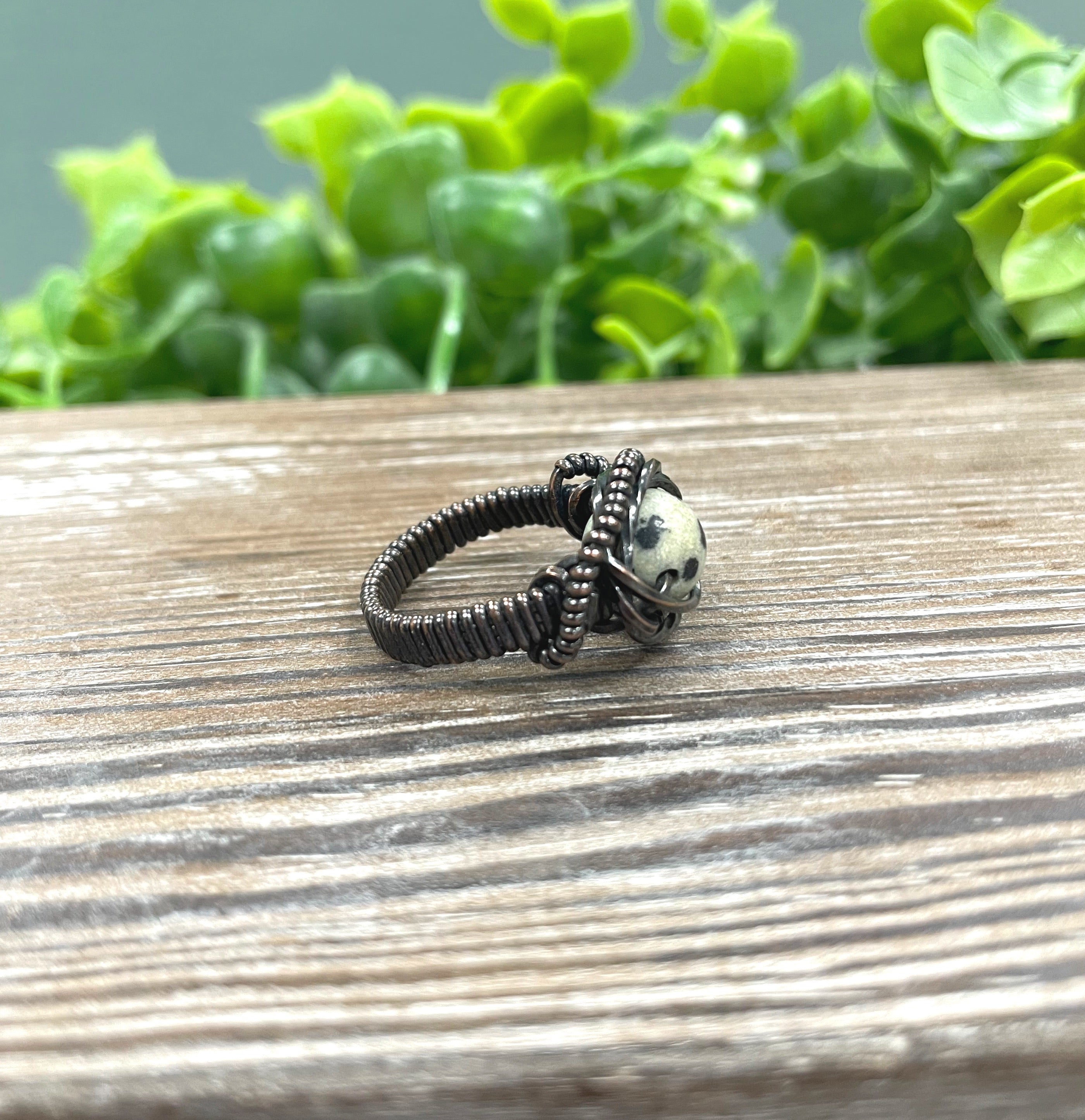 A beautifully crafted Dalmatian Jasper Wire Wrapped Ring featuring a unique spotted bead wrapped in oxidized copper wire, showcasing an antique finish.