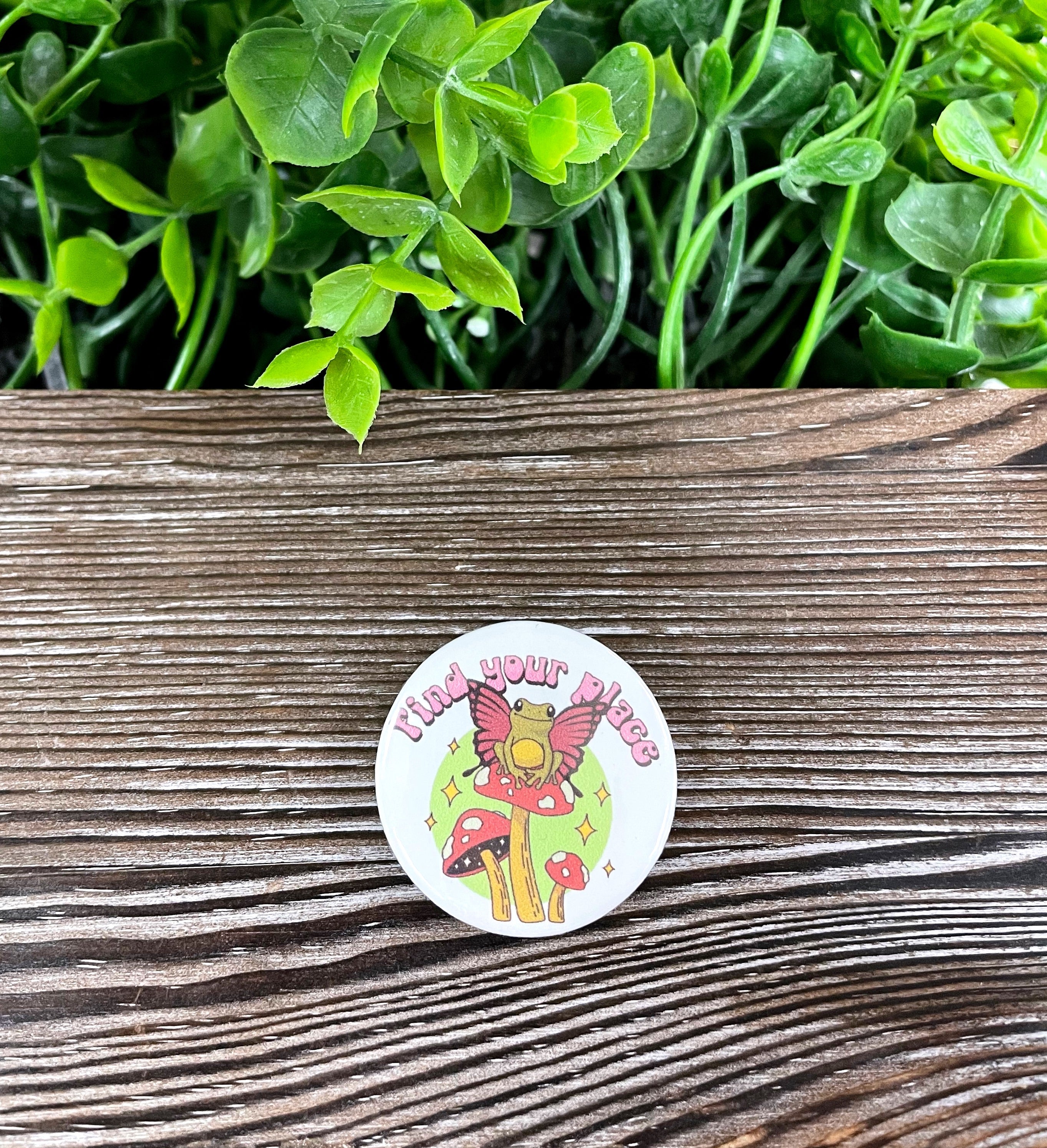 A vibrant 1.25” button featuring a whimsical frog sitting on a mushroom, showcasing a unique graphic art design.
