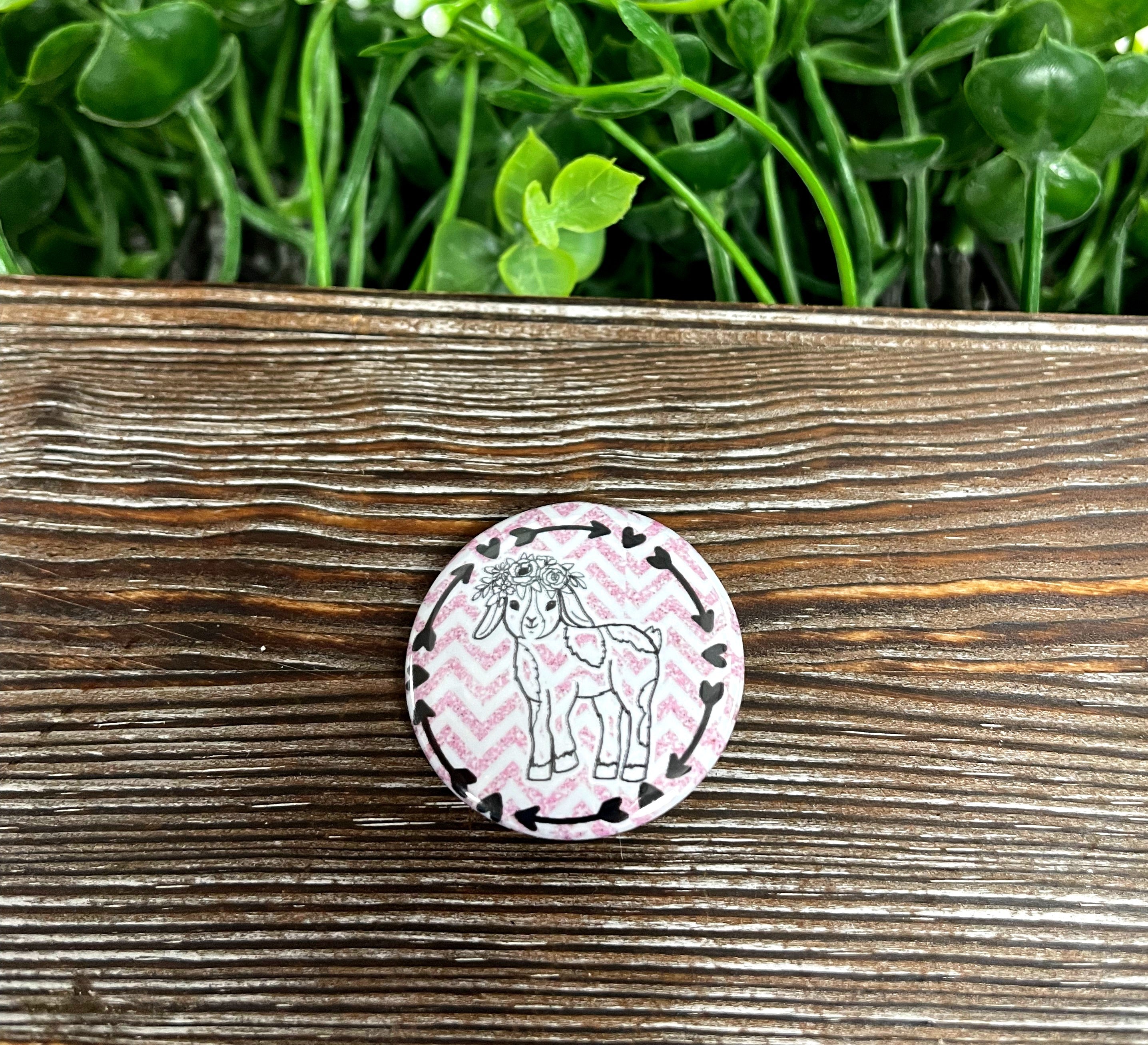 A 1.25-inch graphic art button featuring a goat with a flower crown in pink and white colors, perfect for personal accessories.