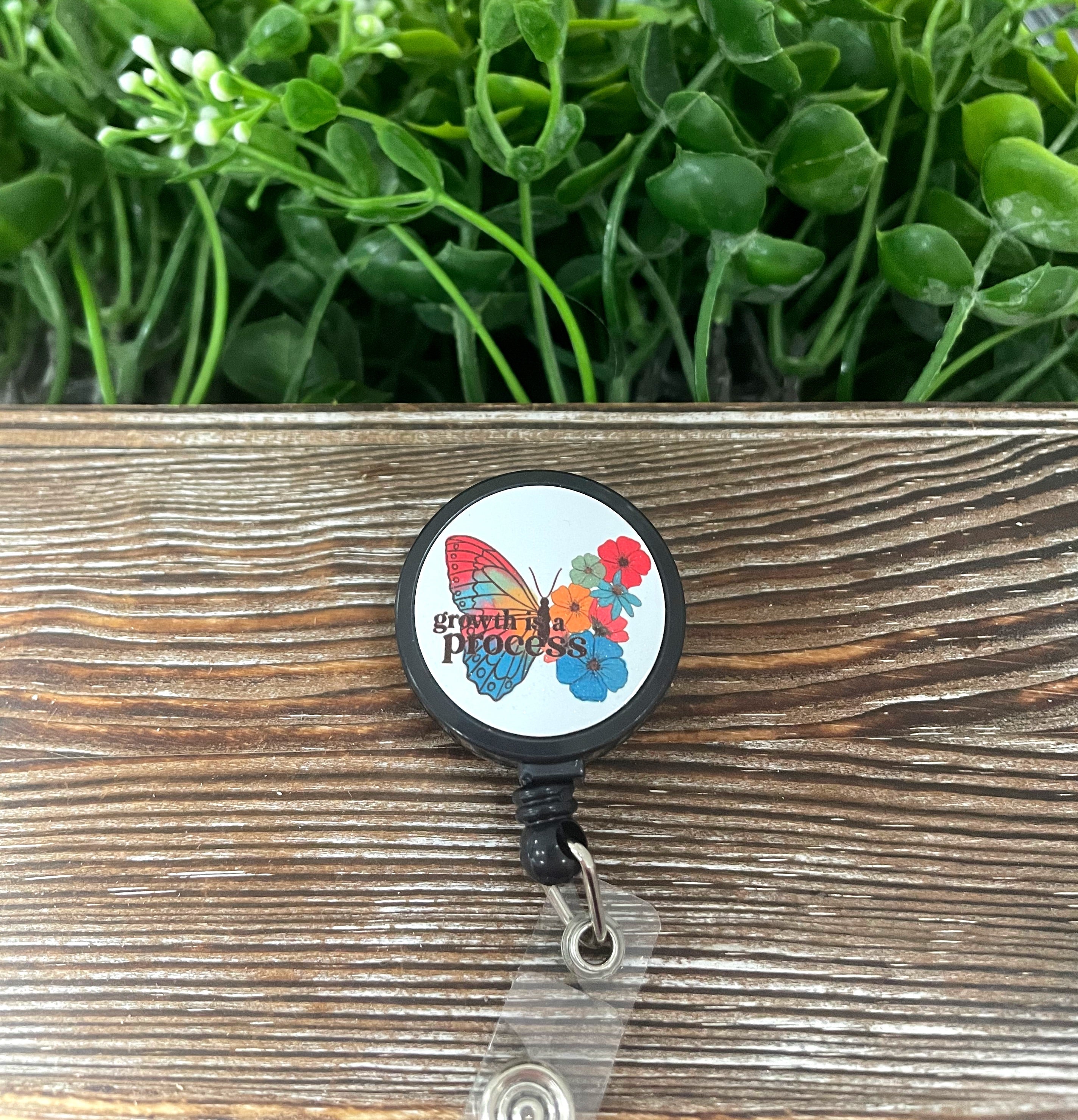 A retractable badge reel featuring a colorful butterfly design, measuring 1.2 inches in diameter with a 24-inch extension cord.