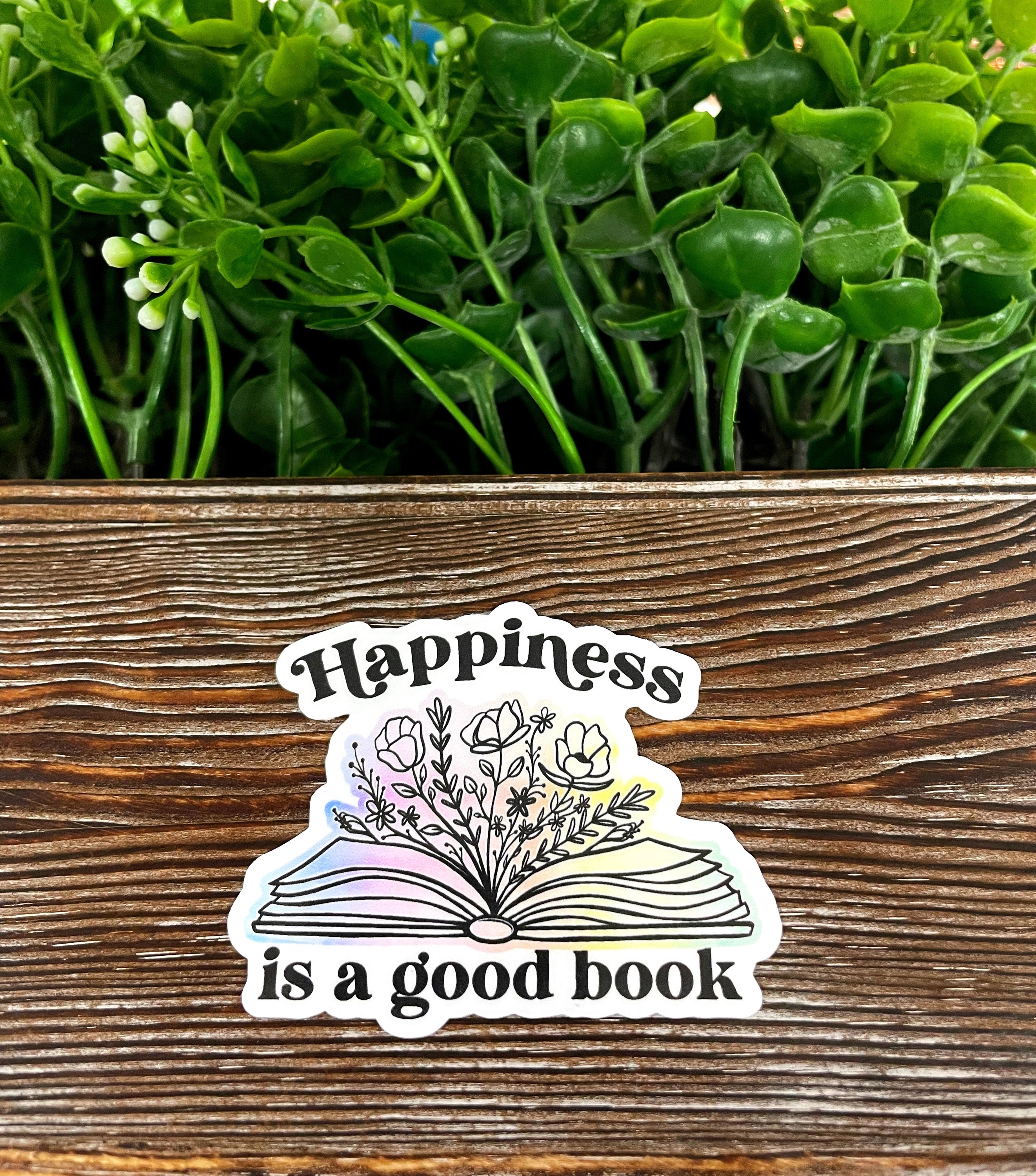 Happiness is a Good Book die cut sticker on a smooth surface, showcasing vibrant colors and a fun design.