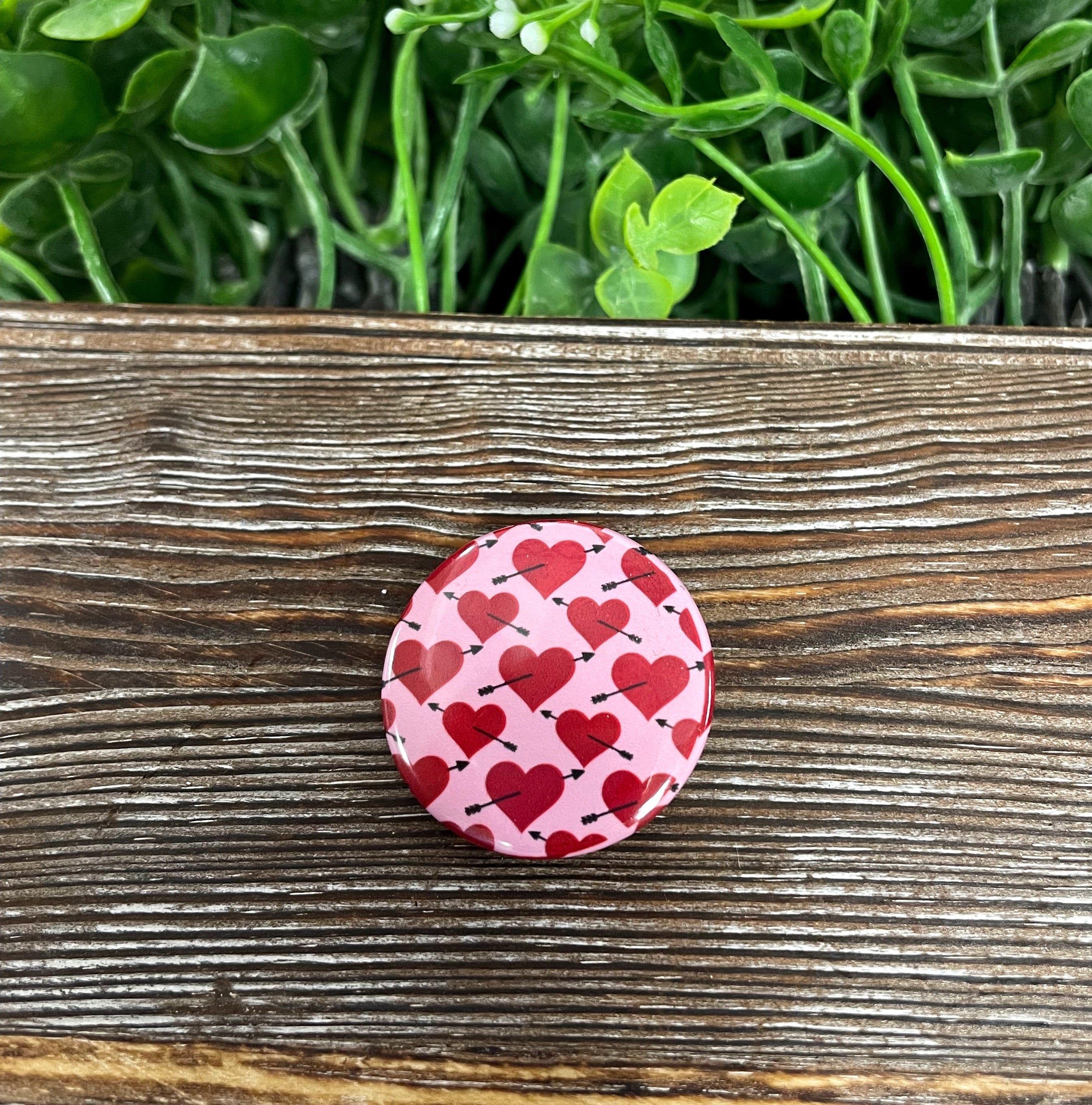 A colorful 1.25-inch button pin featuring hearts and arrows design, perfect for personalizing bags and accessories.