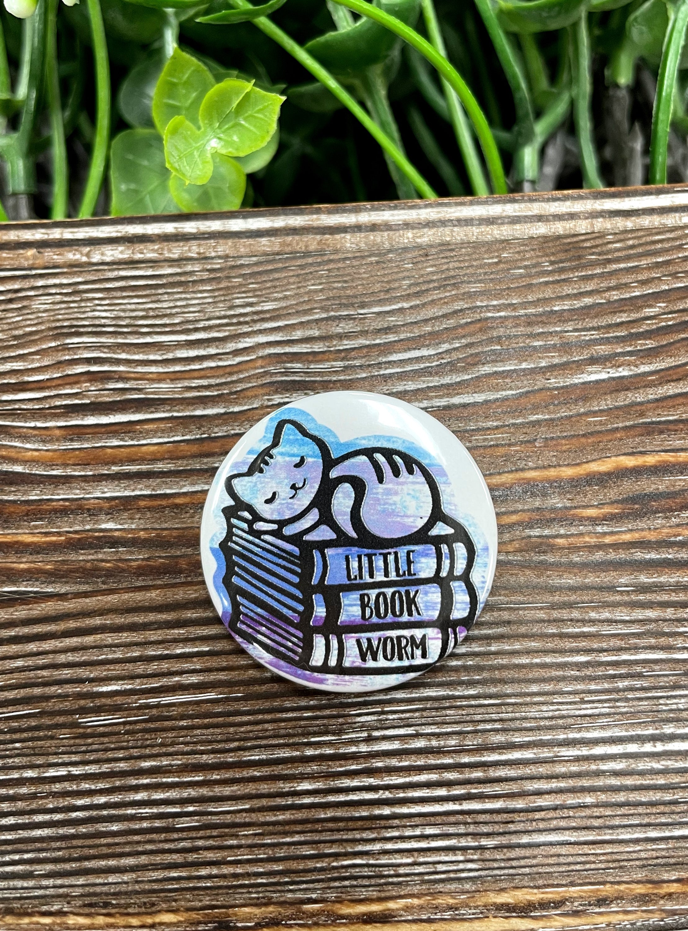 A 1.25-inch button featuring a cute cat graphic with a book, perfect for cat lovers and book enthusiasts.