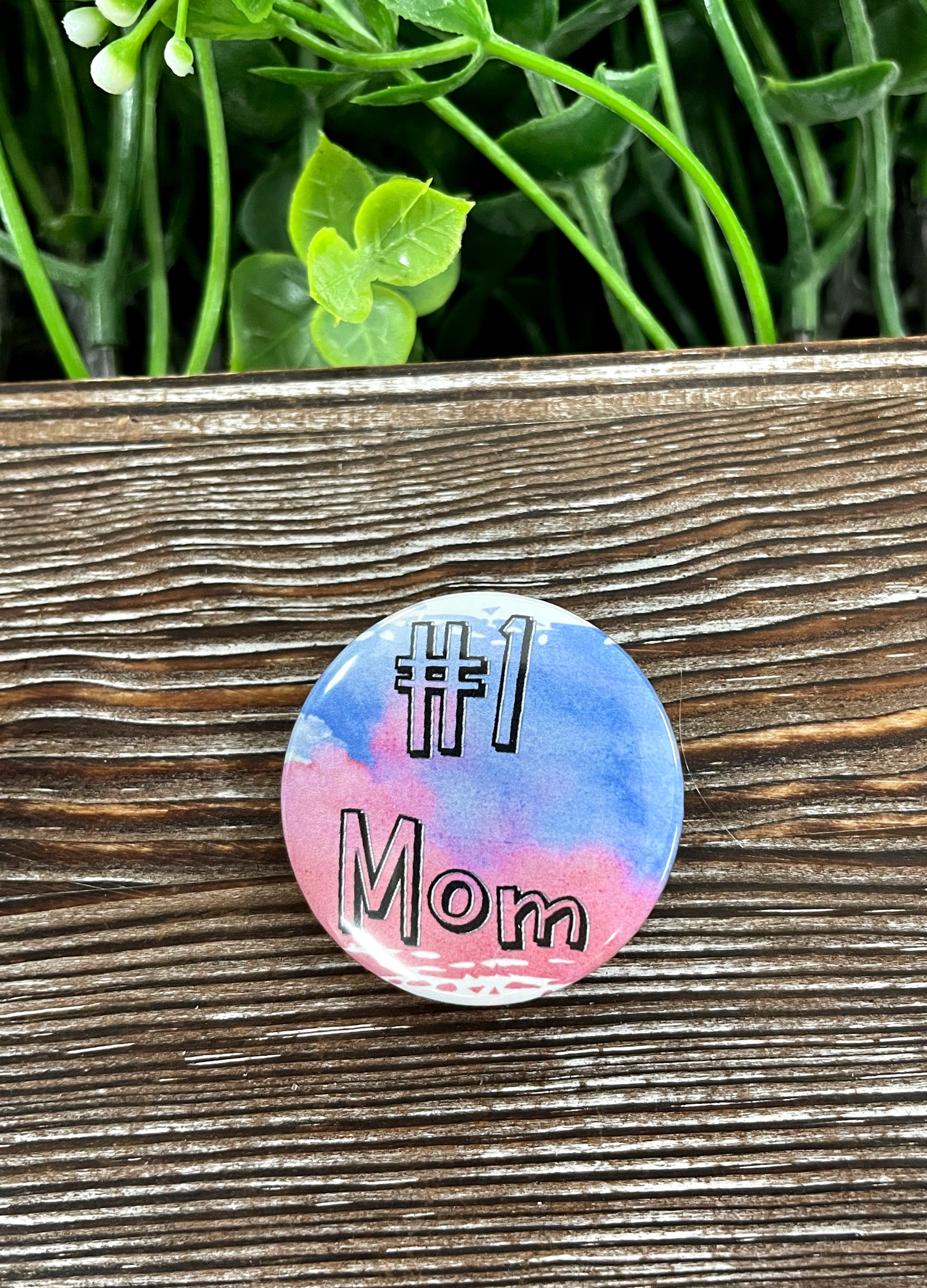 A vibrant 1.25-inch button featuring the text 'Number One Mom #1' with a colorful graphic design, suitable for bags and accessories.