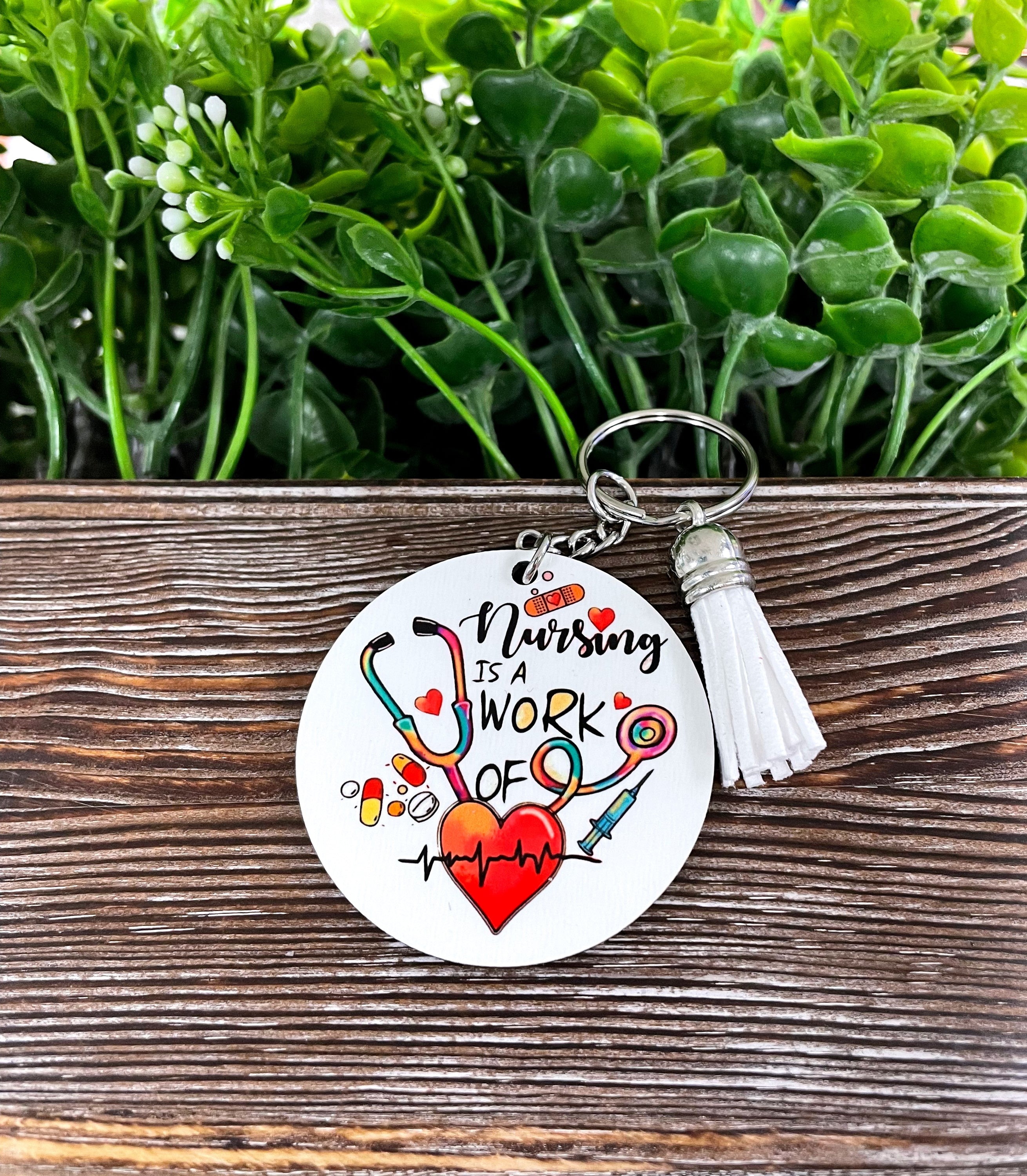A lightweight MDF round keychain featuring a colorful tassel, designed for nursing enthusiasts, showcasing the phrase 'Nursing is a Work of Heart'.