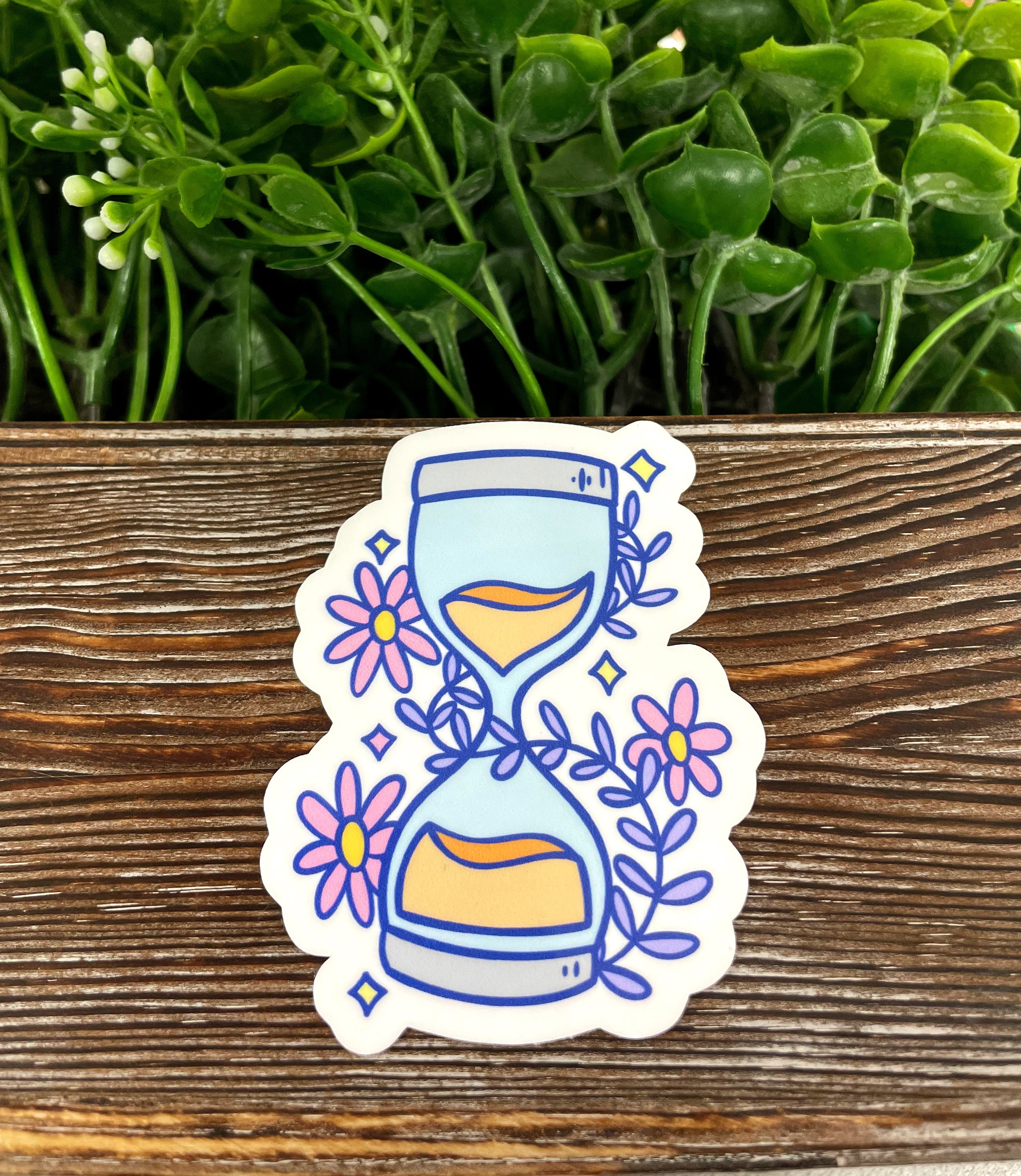Pastel hourglass die cut sticker on a smooth surface, showcasing vibrant colors and a unique design.