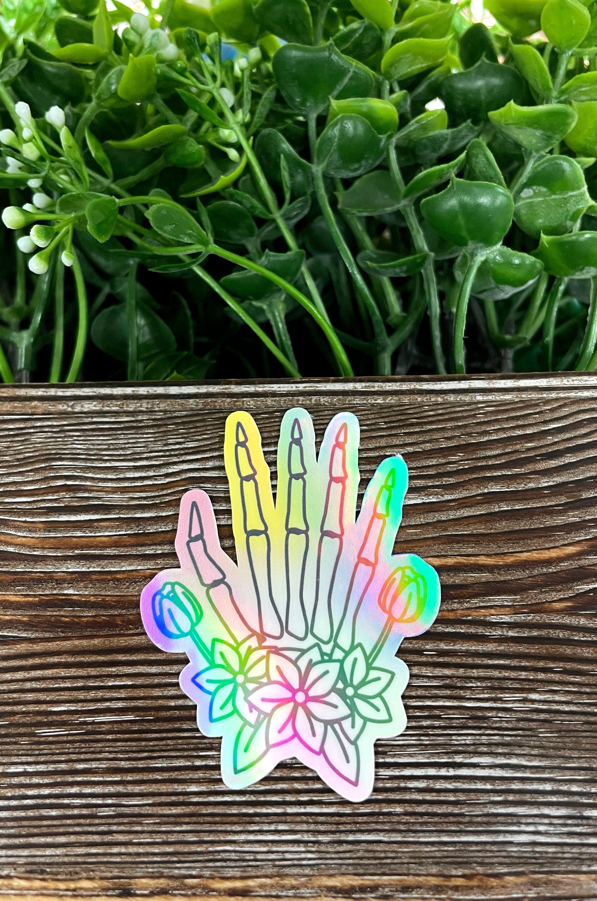 Pastel watercolor skeletal hand die cut vinyl sticker on a smooth surface, showcasing vibrant colors and intricate design.