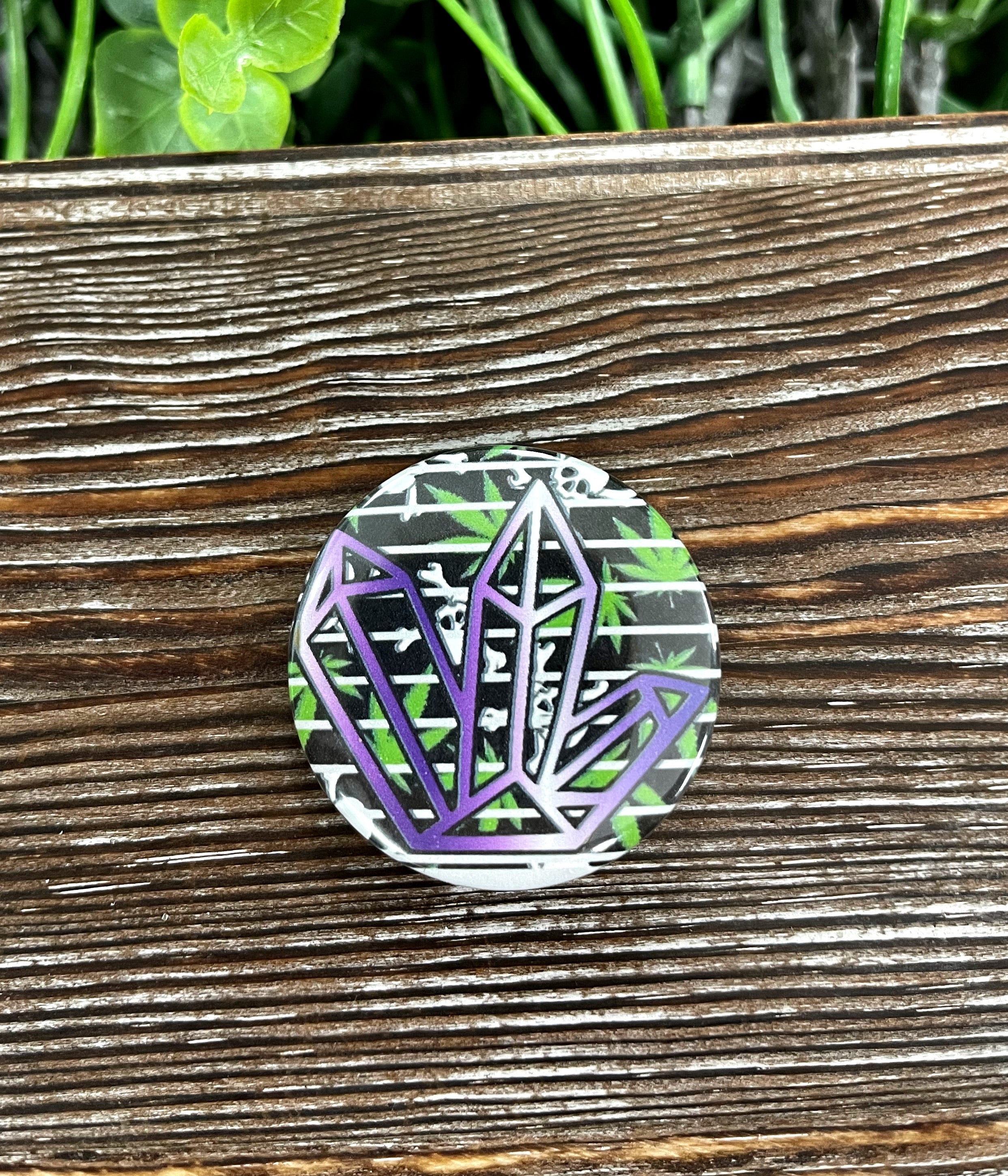 A vibrant 1.25-inch button featuring a purple and green crystal gemstone graphic design, perfect for personalizing accessories.