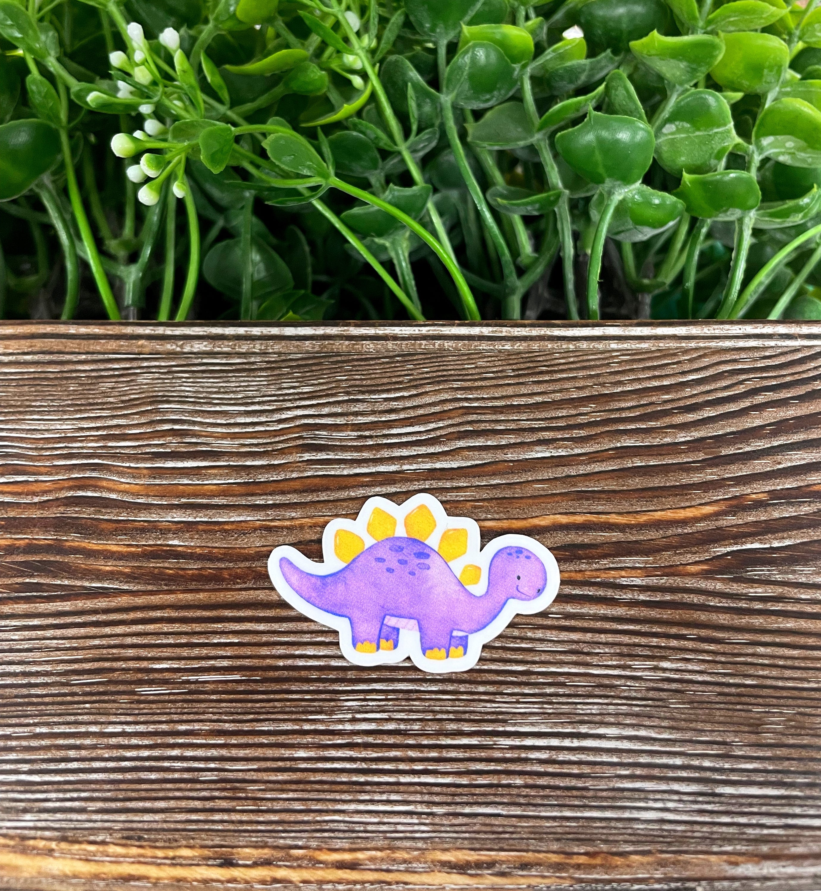 Purple watercolor dinosaur die cut vinyl sticker on a smooth surface, showcasing vibrant colors and intricate design.