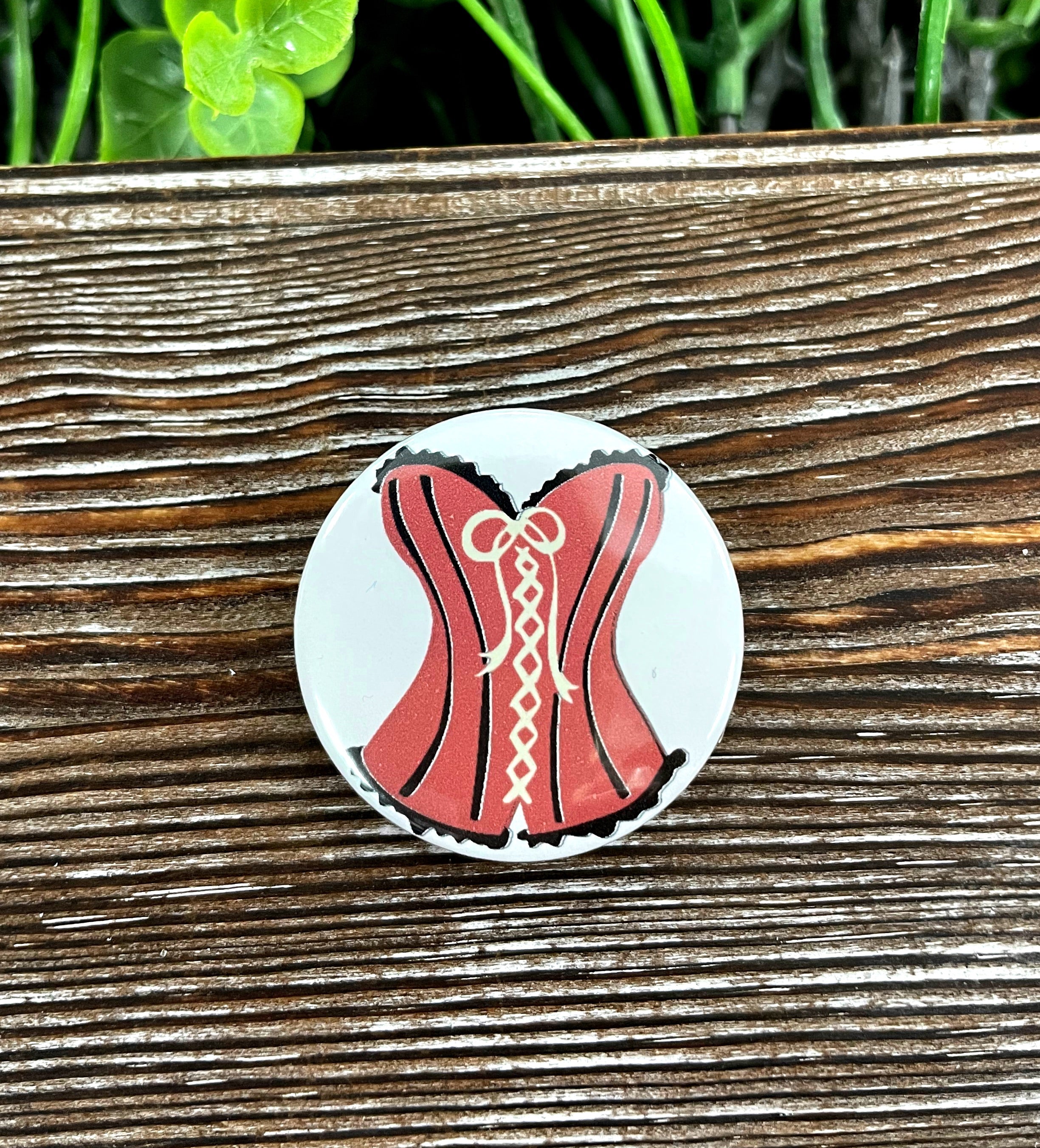 A stylish 1.25-inch button featuring a sexy laced corset graphic design, perfect for personal expression.