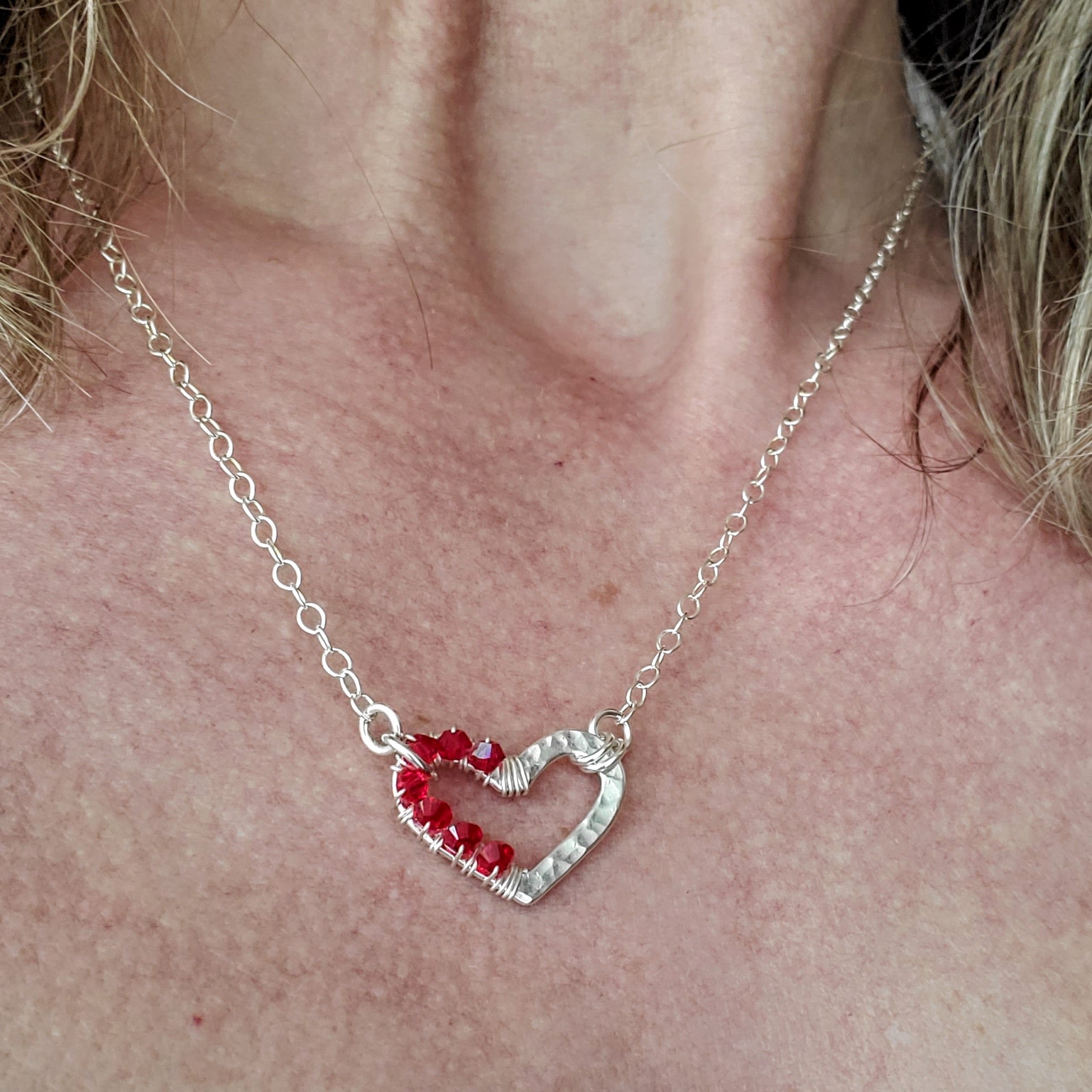 A beautiful silver necklace featuring a hammered heart pendant adorned with red Swarovski crystals, showcasing elegance and craftsmanship.