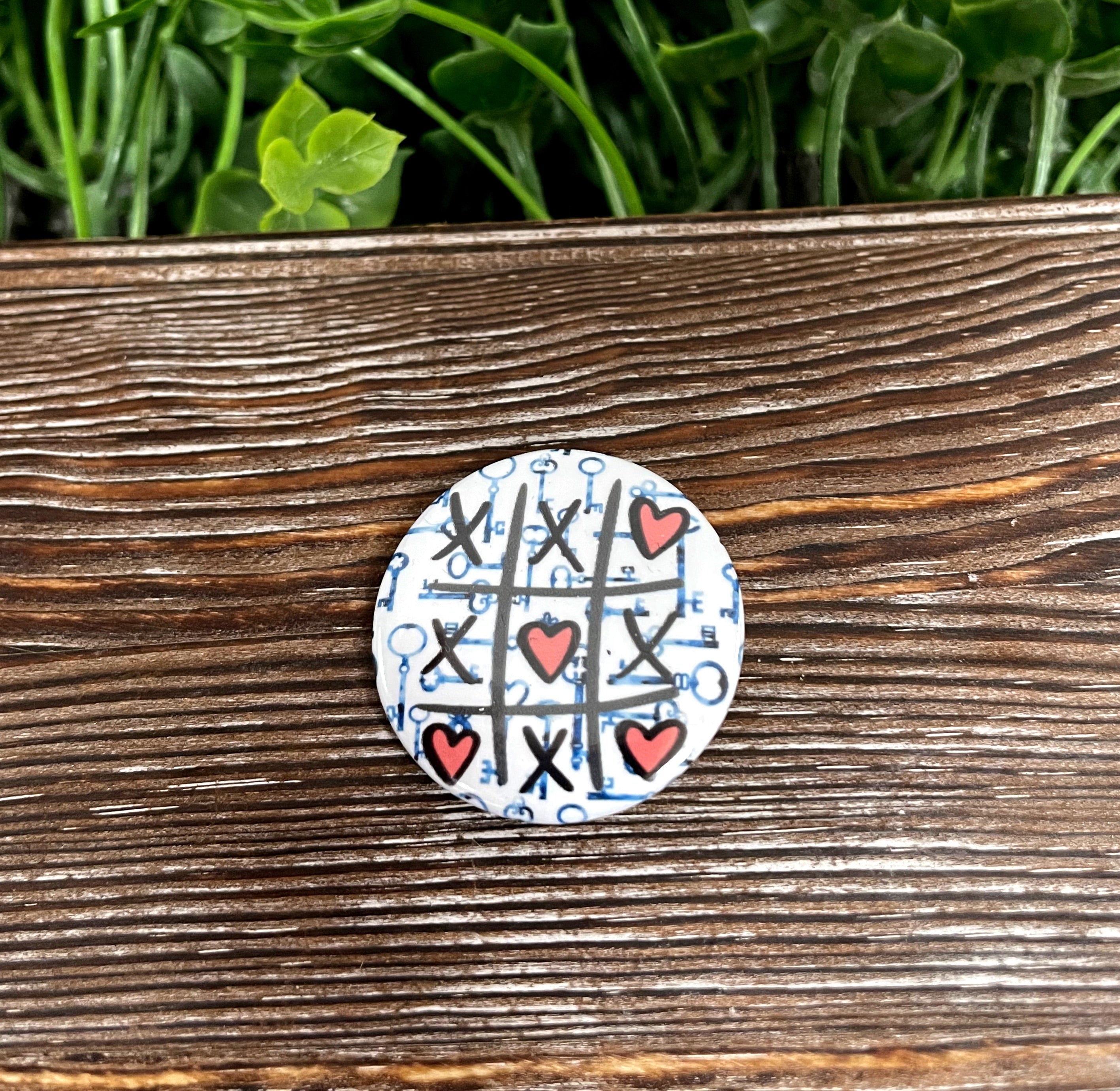 A colorful 1.25-inch Tic Tac Toe Hearts Graphic Art Button featuring a playful design, perfect for accessorizing bags and clothing.