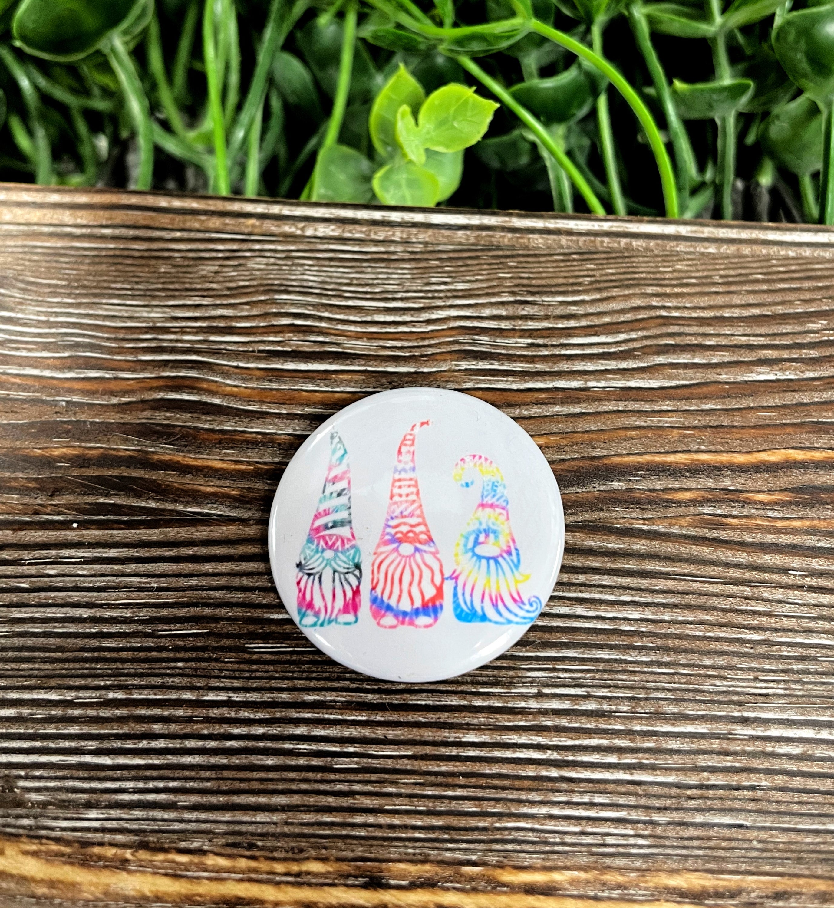 A colorful Tie Dye Gnome Trio graphic art button pin, measuring 1.25 inches, featuring playful gnome designs.