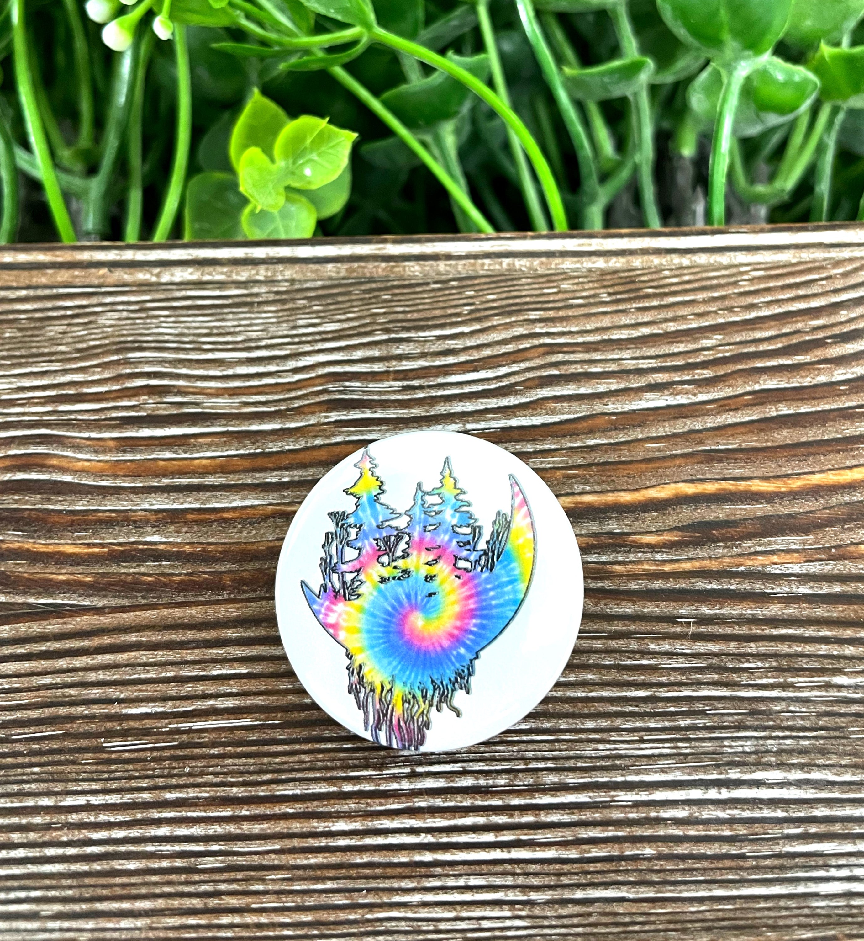 A colorful tie dye button featuring tree roots and a moon graphic, measuring 1.25 inches in diameter.