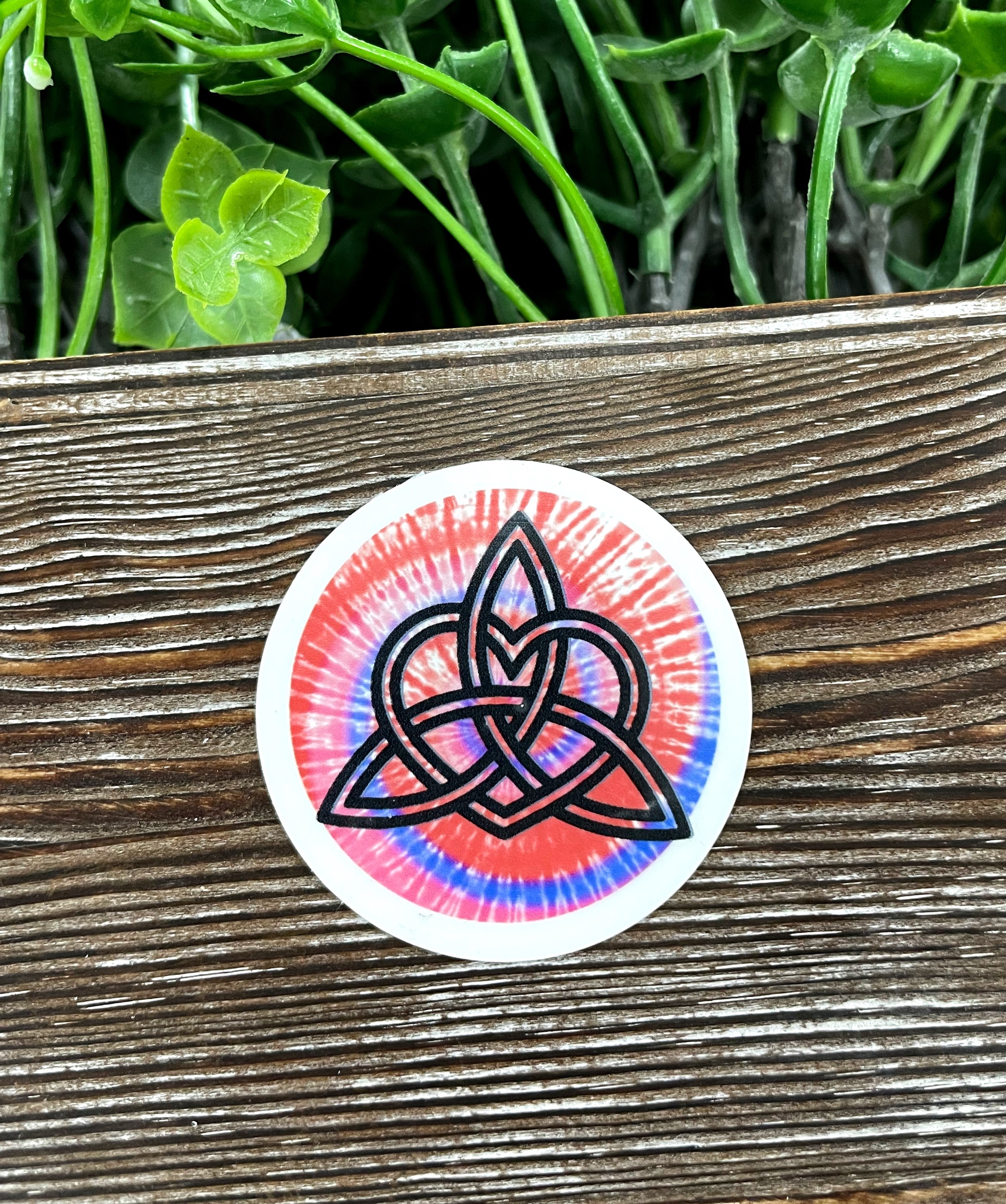 Colorful Tie Dye Triquetra Die Cut Sticker on a smooth surface, showcasing vibrant colors and intricate design.