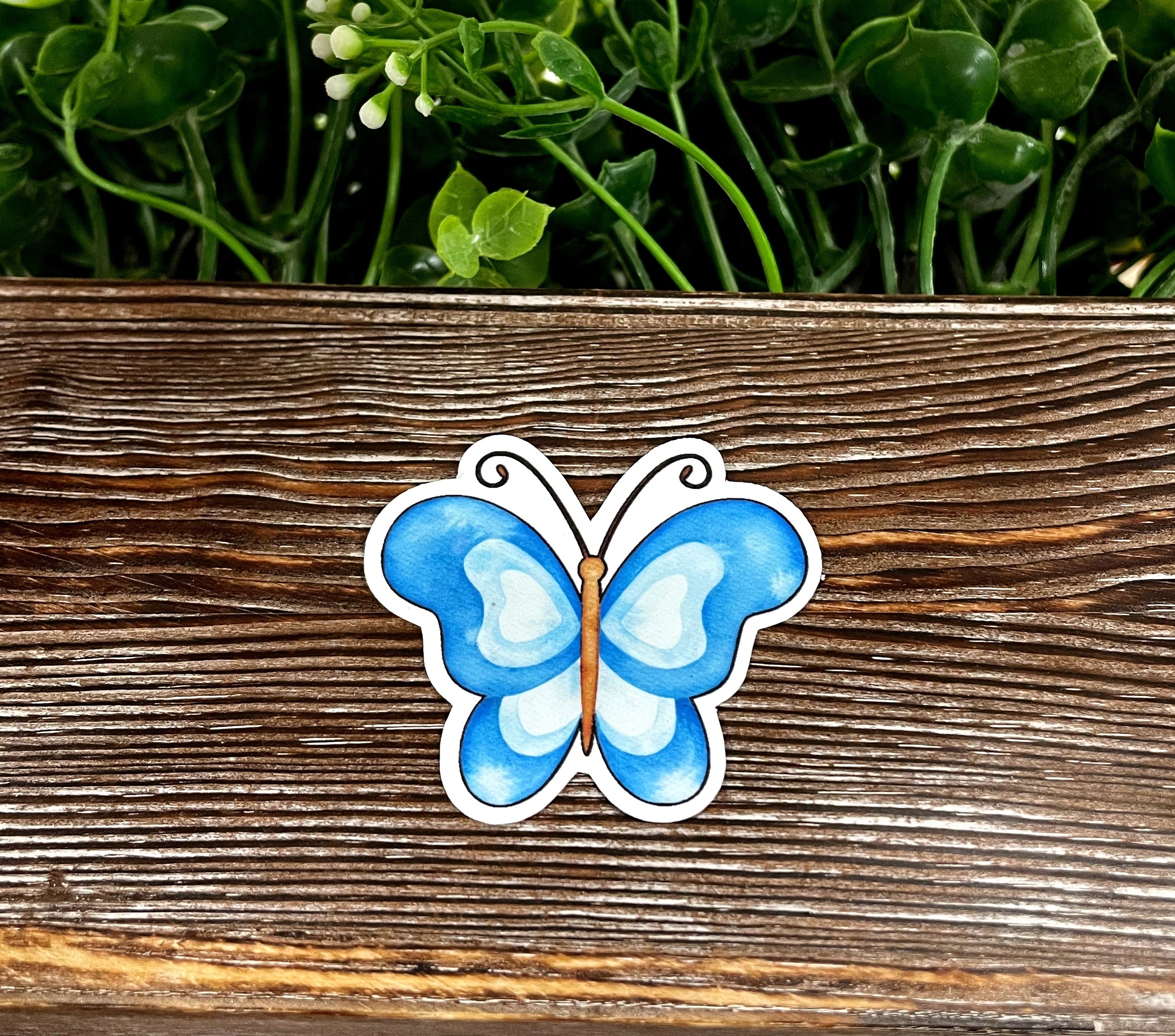 A vibrant watercolor blue butterfly sticker on a smooth surface, showcasing intricate details and colors.