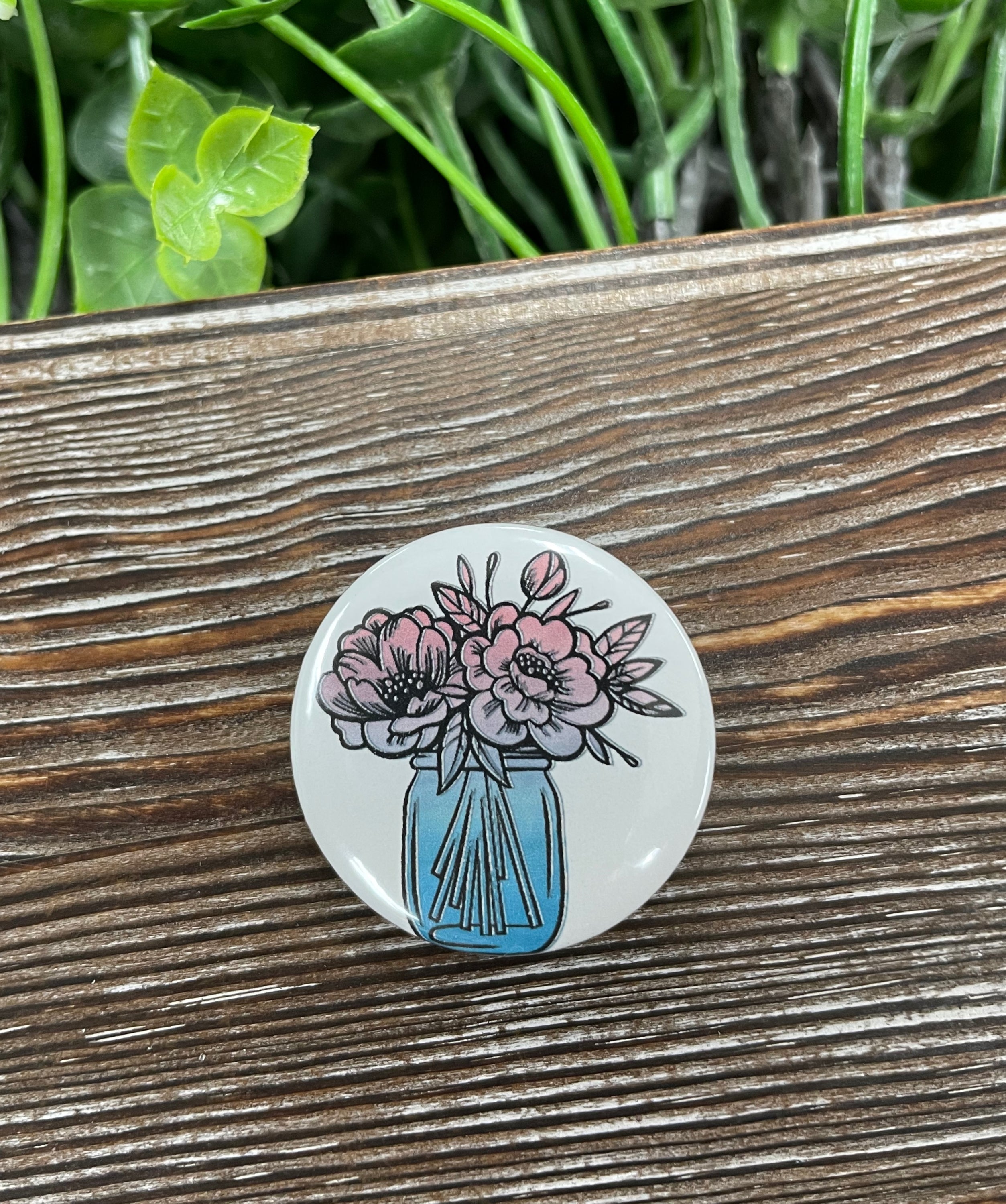 A colorful 1.25-inch button featuring watercolor flowers in a mason jar design, perfect for personalizing bags and accessories.