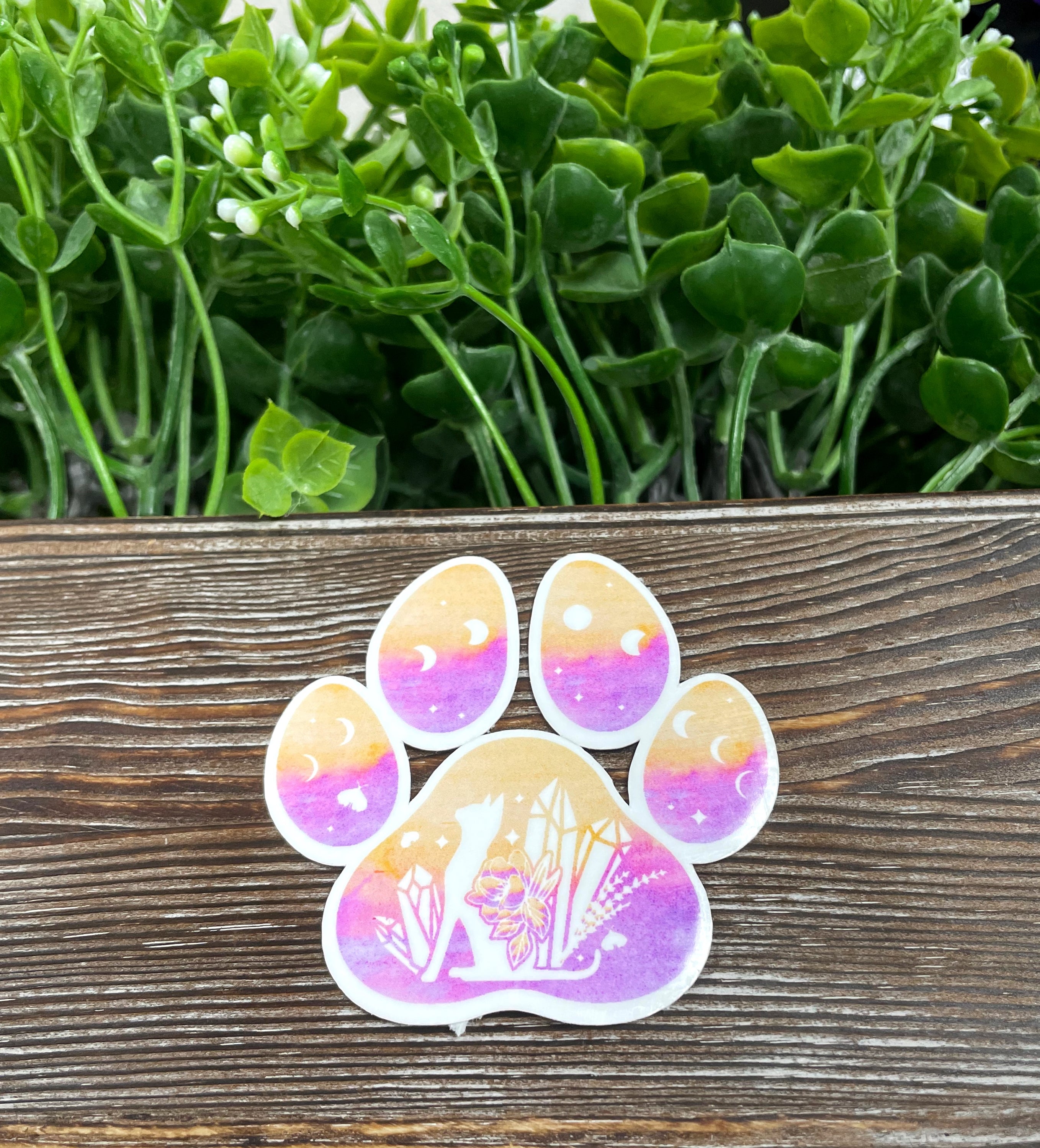 A vibrant watercolor paw print die cut sticker on a smooth surface, showcasing its artistic design and colors.