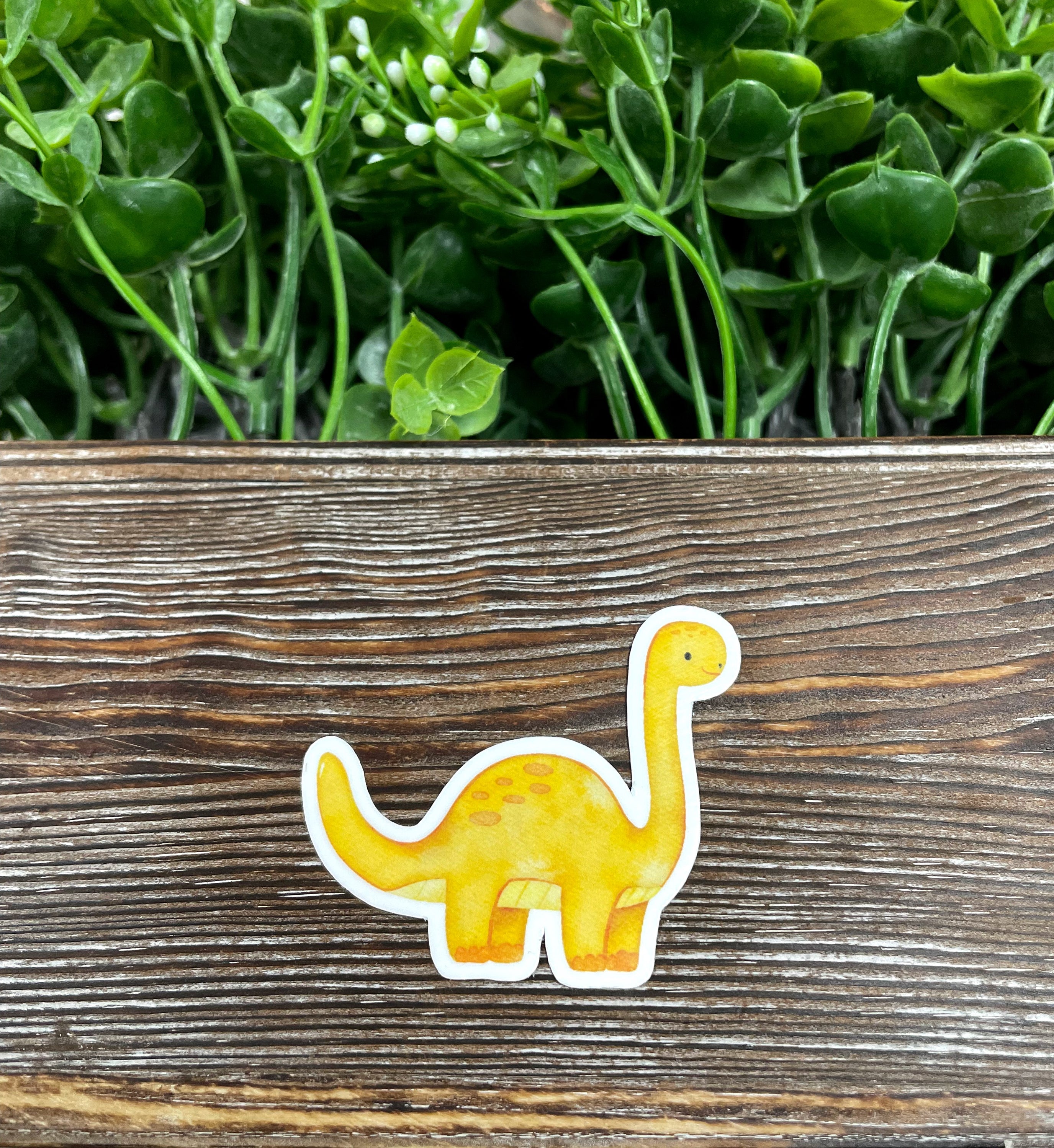A vibrant watercolor yellow dinosaur die cut sticker featuring a long neck design, perfect for personalizing various surfaces.