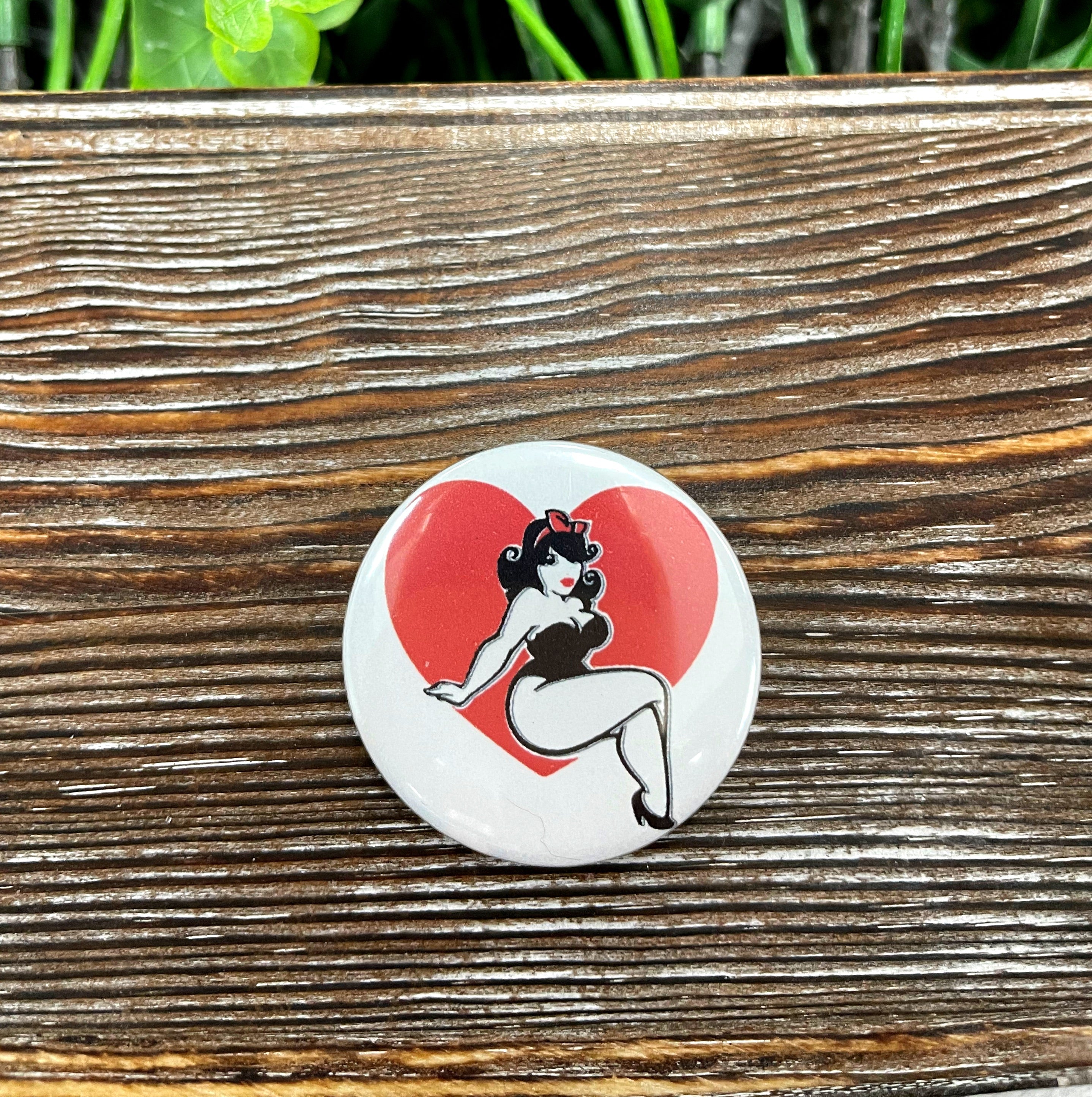 A vibrant 1.25-inch Woman Pinup Heart Graphic Art Button with a plastic back, showcasing a charming pinup heart design.