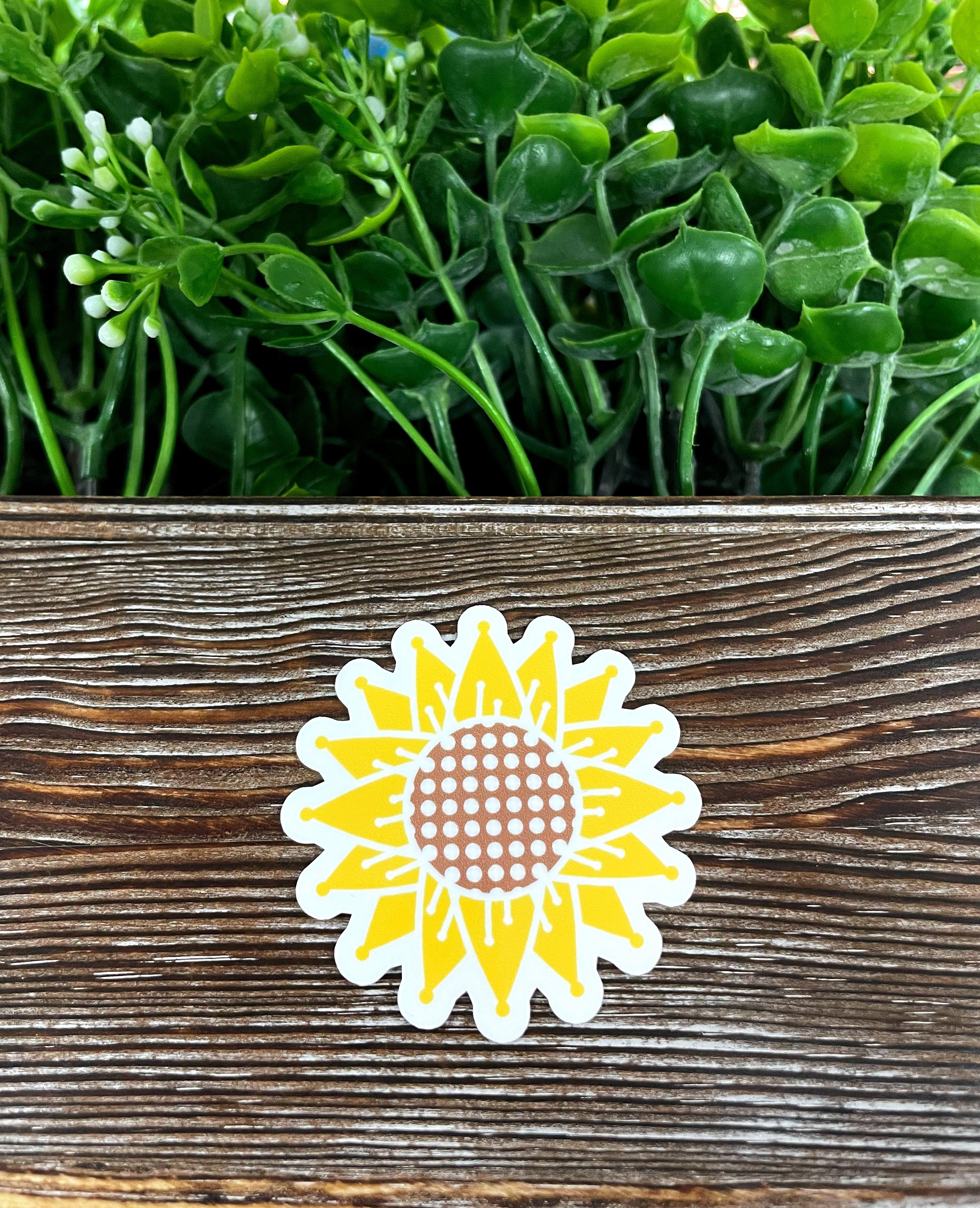 A vibrant yellow sunflower die cut vinyl sticker on a smooth surface, showcasing its intricate design and water-resistant laminate finish.