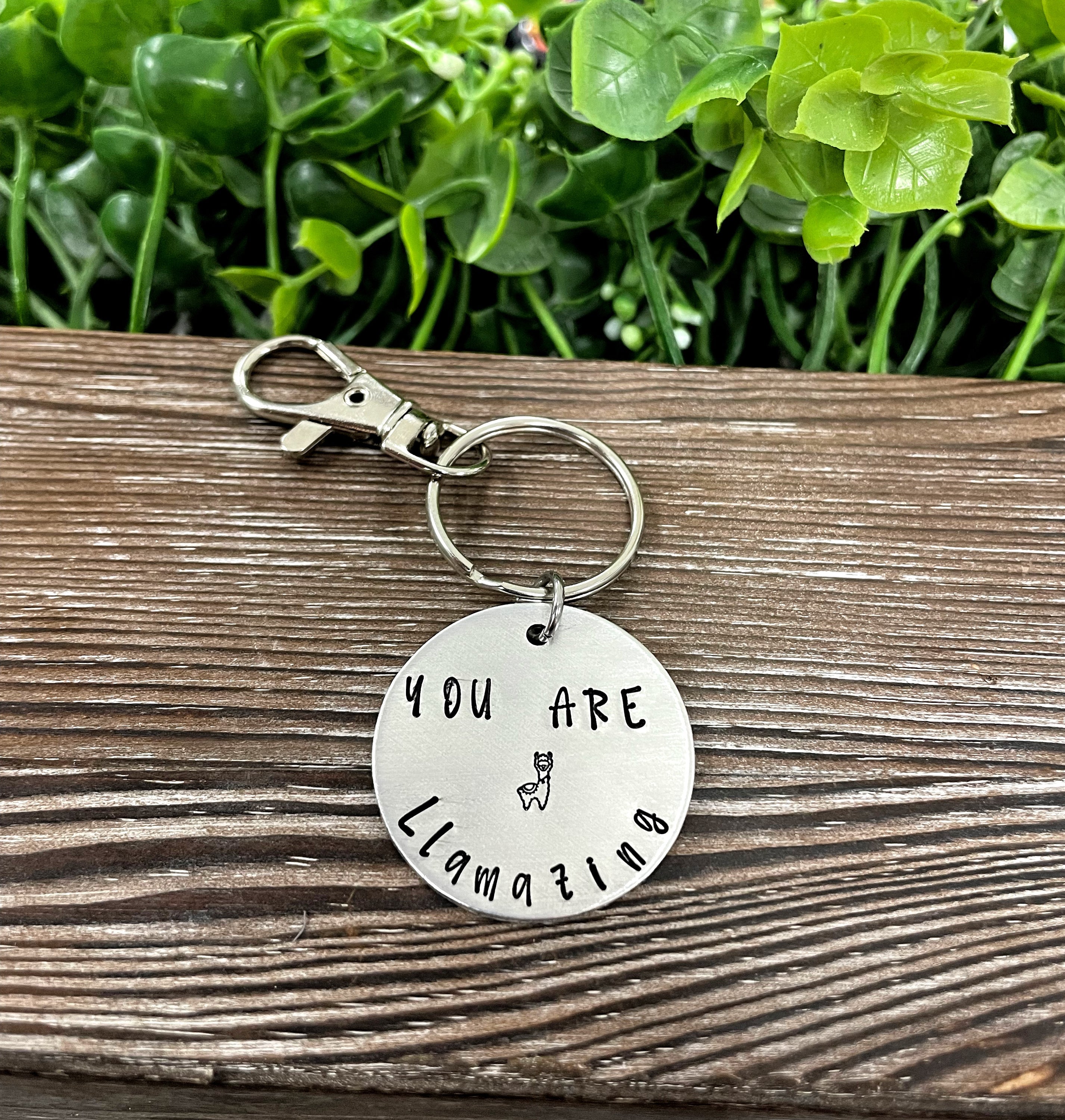 Hand-stamped keychain featuring a llama design with the phrase 'You Are Llamazing', showcasing unique variations.