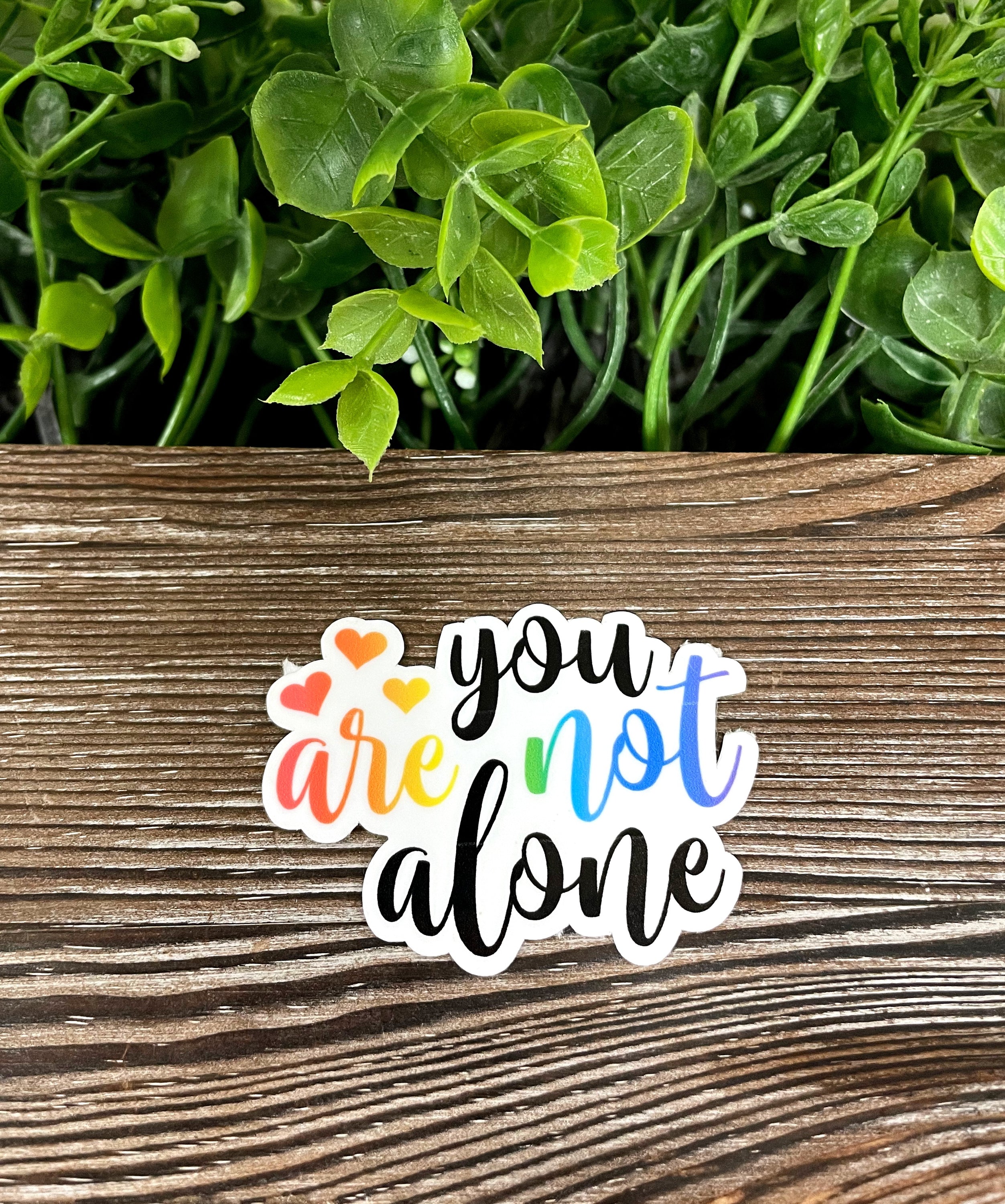 A vibrant 'You Are Not Alone' die cut vinyl sticker featuring boho fun design, water resistant and perfect for personalizing various surfaces.