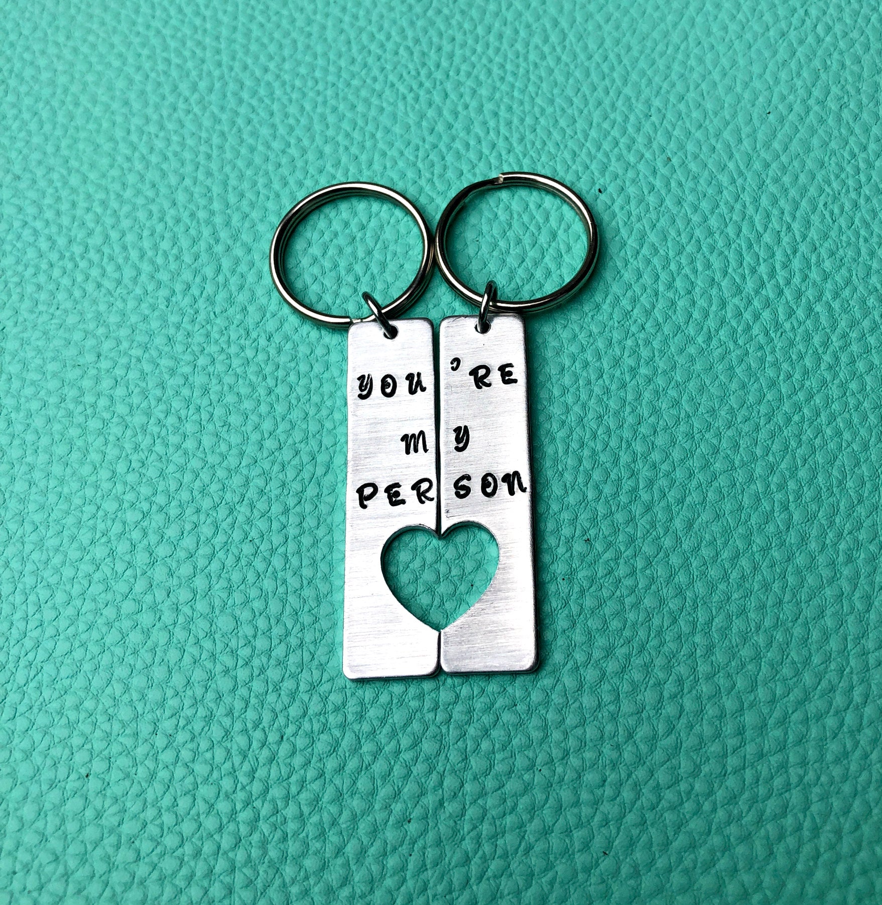 Hand-stamped You're My Person Key Chains showcasing unique letters and designs, perfect for anniversaries.