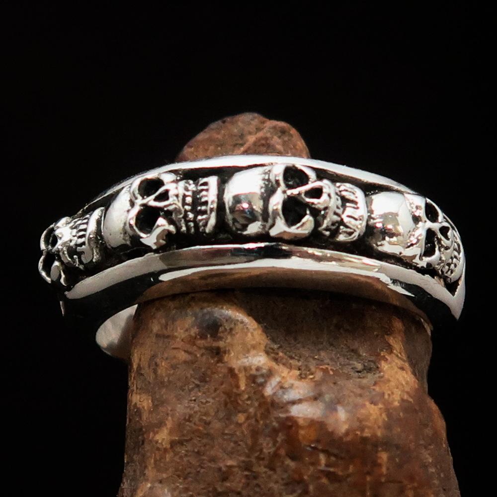 Men's sterling silver band ring featuring four small skulls, high polished and antiqued finish, showcasing intricate details.