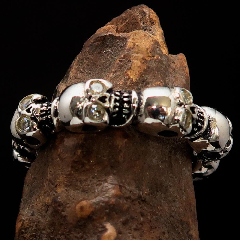Men's sterling silver band ring featuring 6 small skulls with white cubic zirconia eyes, showcasing a polished and antiqued finish.
