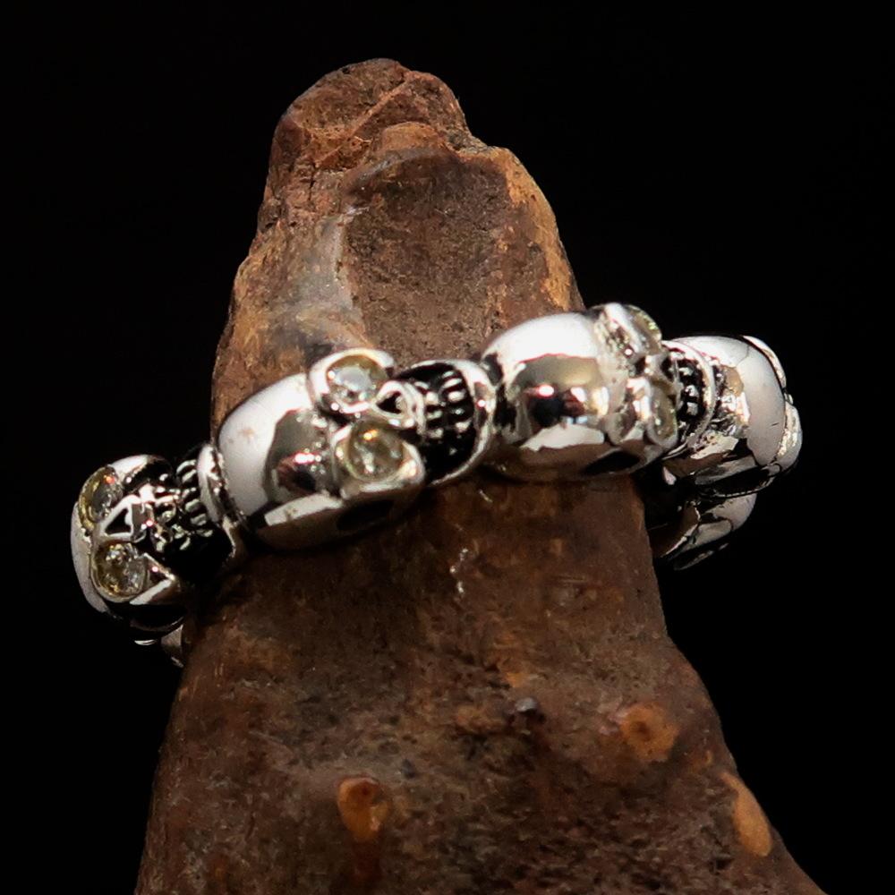 Men's sterling silver band ring featuring 6 small skulls with white cubic zirconia eyes, showcasing a polished and antiqued finish.