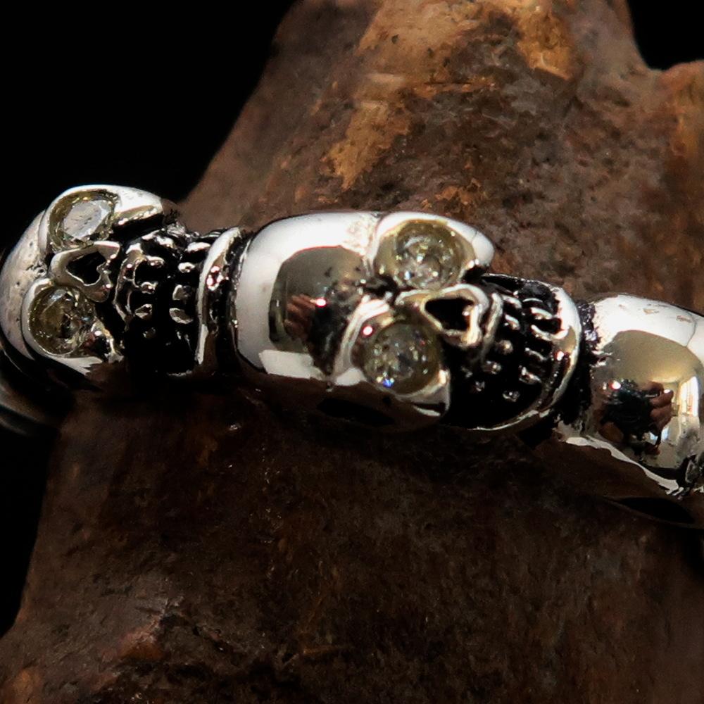 Men's sterling silver band ring featuring 6 small skulls with white cubic zirconia eyes, showcasing a polished and antiqued finish.