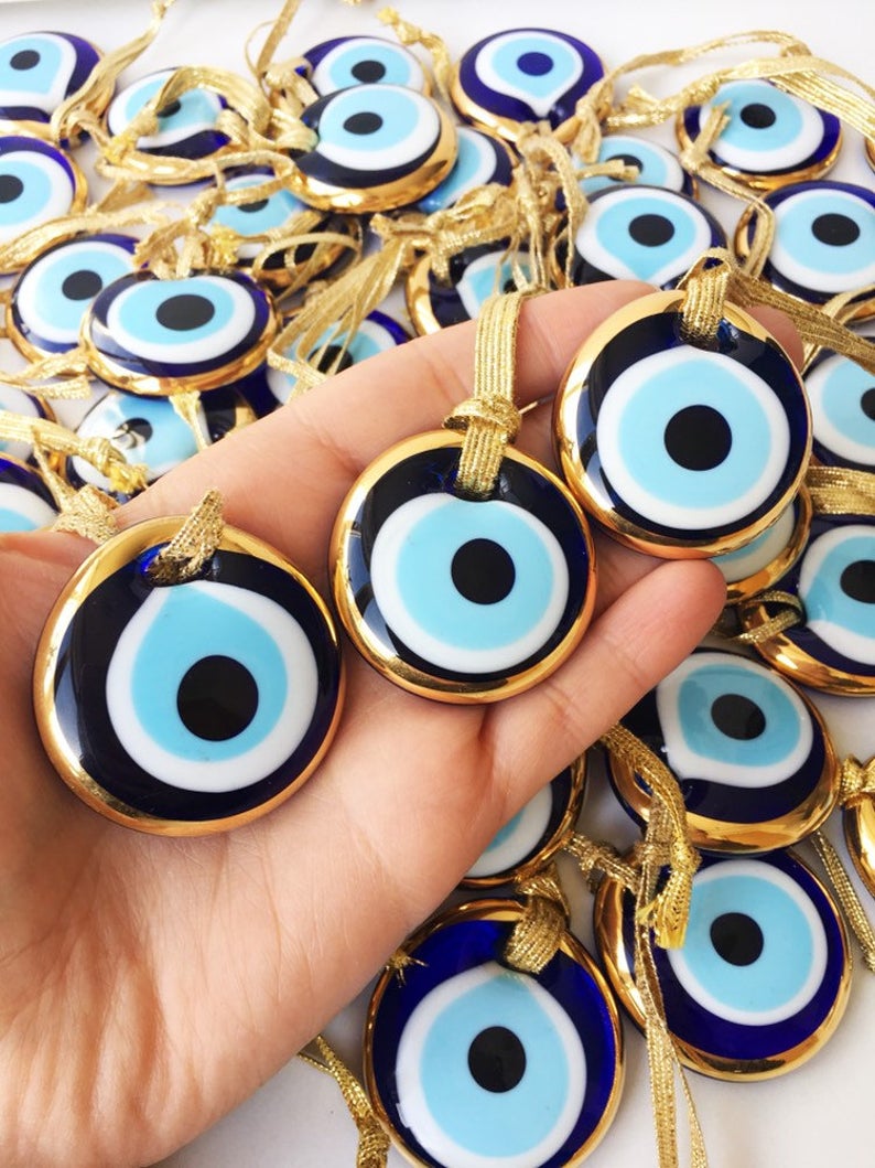 A beautiful gold trimmed glass evil eye bead, featuring a vibrant blue center, perfect for wedding favors and home decor.