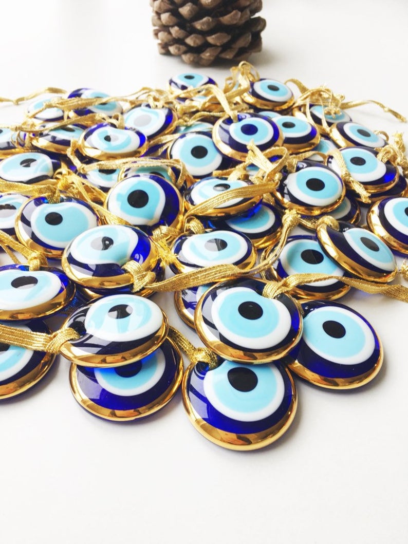 A beautiful gold trimmed glass evil eye bead, featuring a vibrant blue center, perfect for wedding favors and home decor.