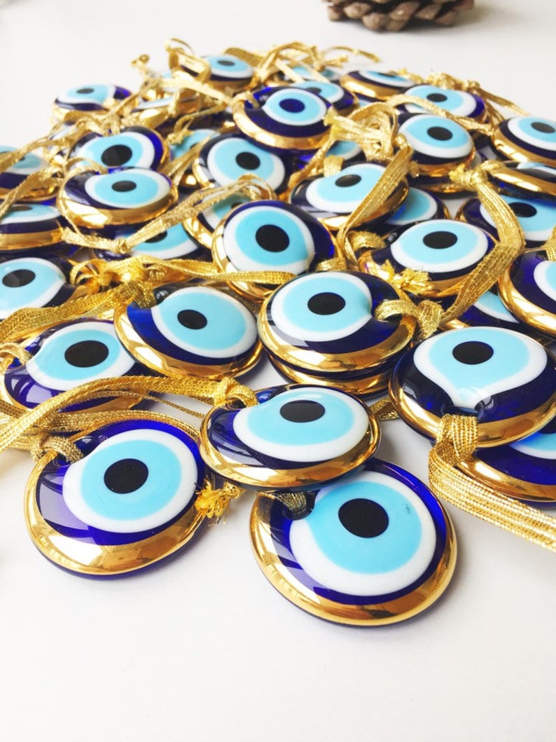 A beautiful gold trimmed glass evil eye bead, featuring a vibrant blue center, perfect for wedding favors and home decor.
