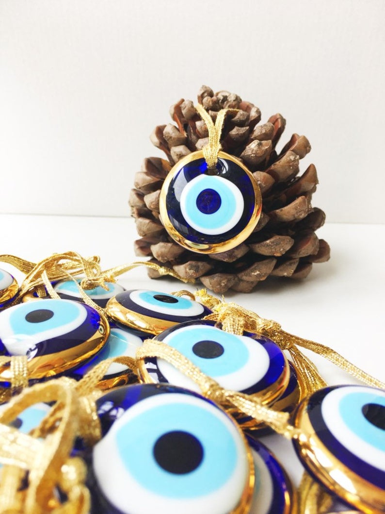 A beautiful gold trimmed glass evil eye bead, featuring a vibrant blue center, perfect for wedding favors and home decor.