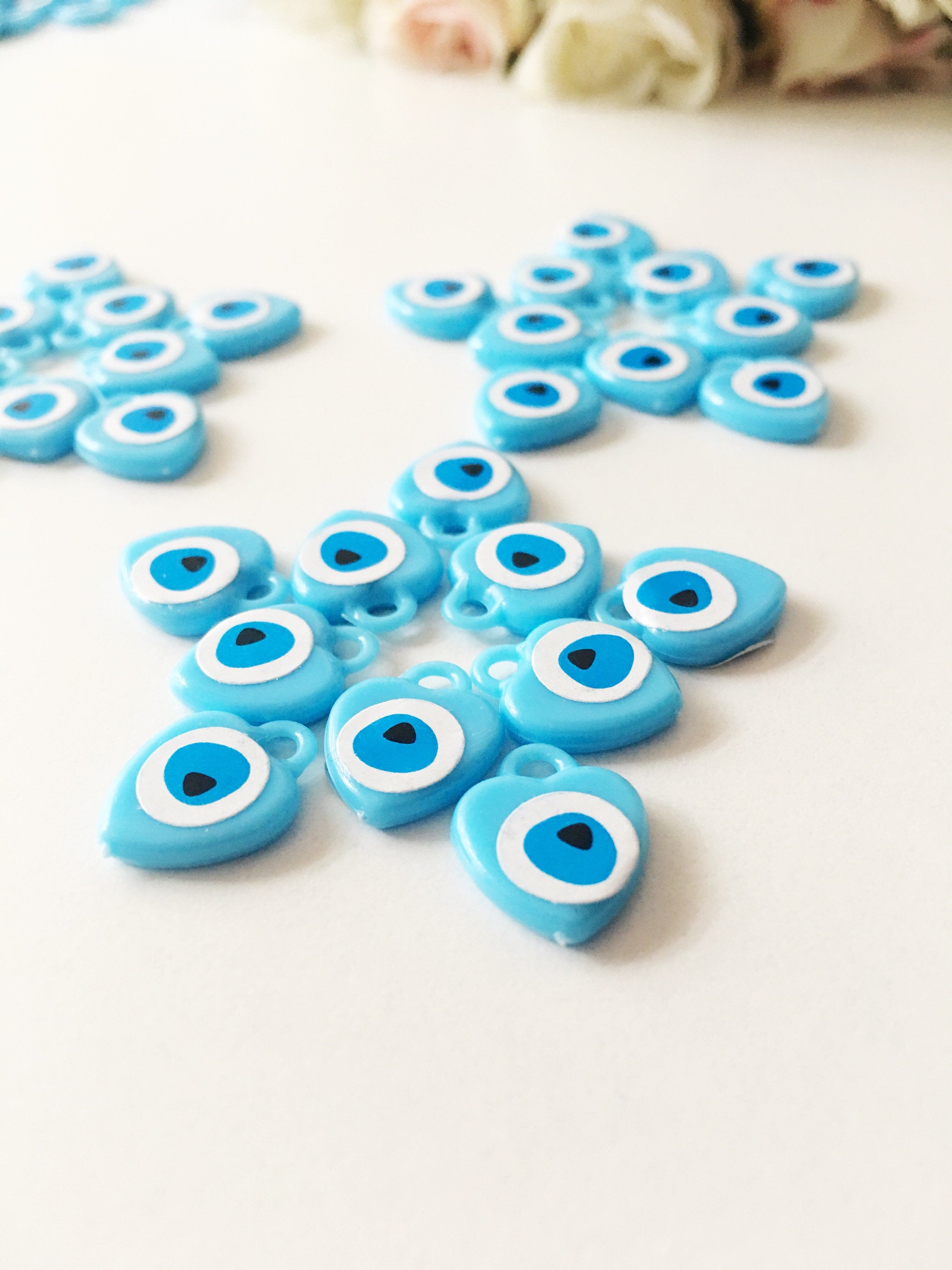 A collection of 100 turquoise evil eye charms made from resin, showcasing their vibrant blue color and unique design, perfect for wedding and baby shower favors.
