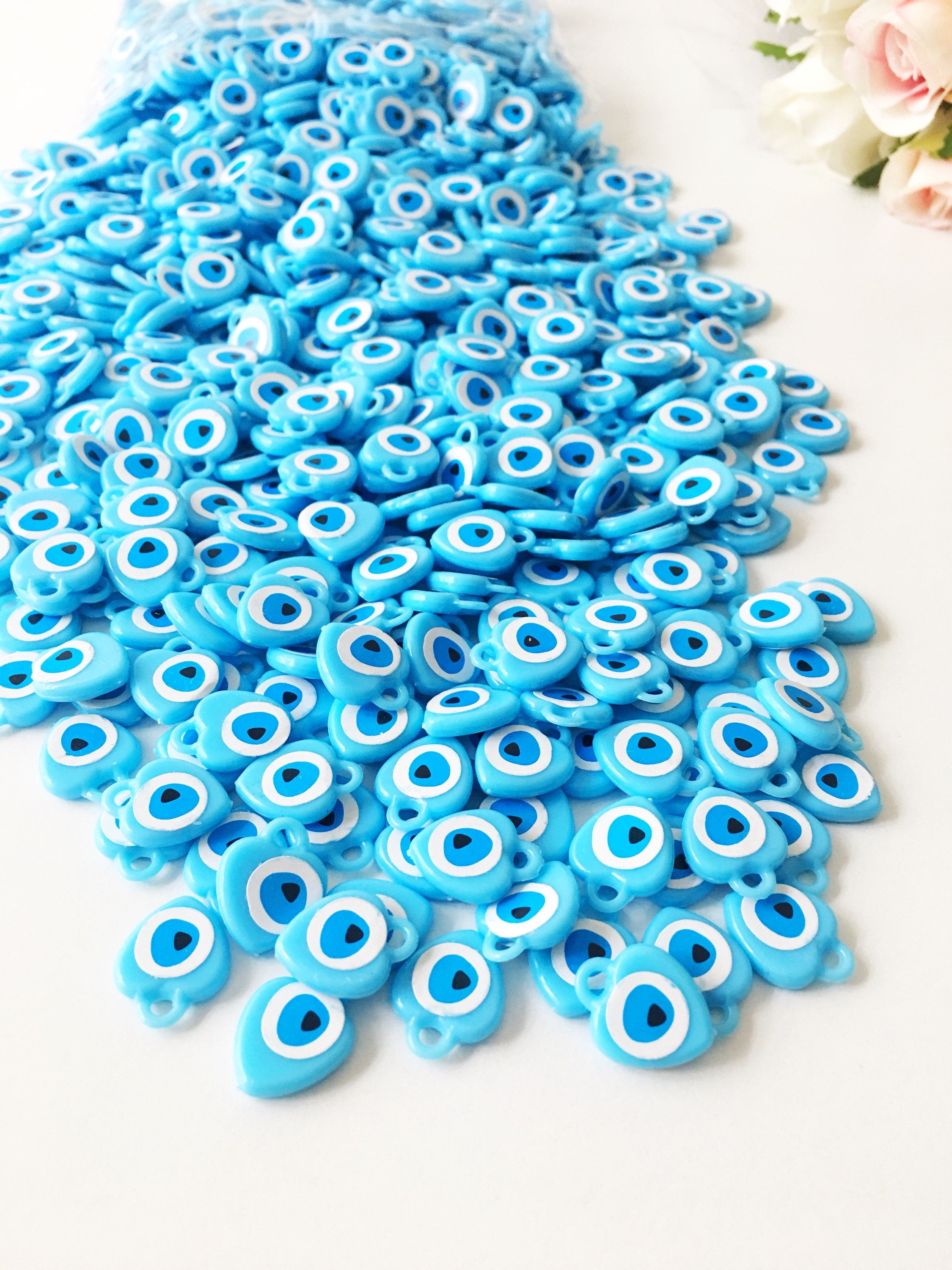 A collection of 100 turquoise evil eye charms made from resin, showcasing their vibrant blue color and unique design, perfect for wedding and baby shower favors.