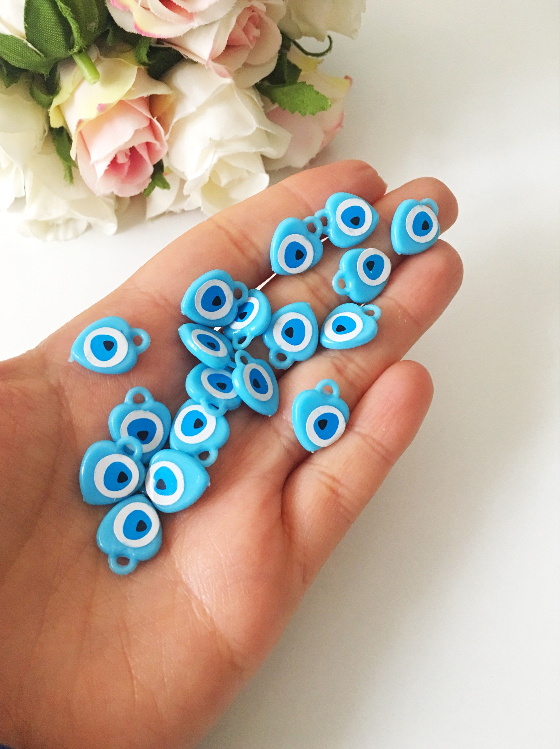 A collection of 100 turquoise evil eye charms made from resin, showcasing their vibrant blue color and unique design, perfect for wedding and baby shower favors.
